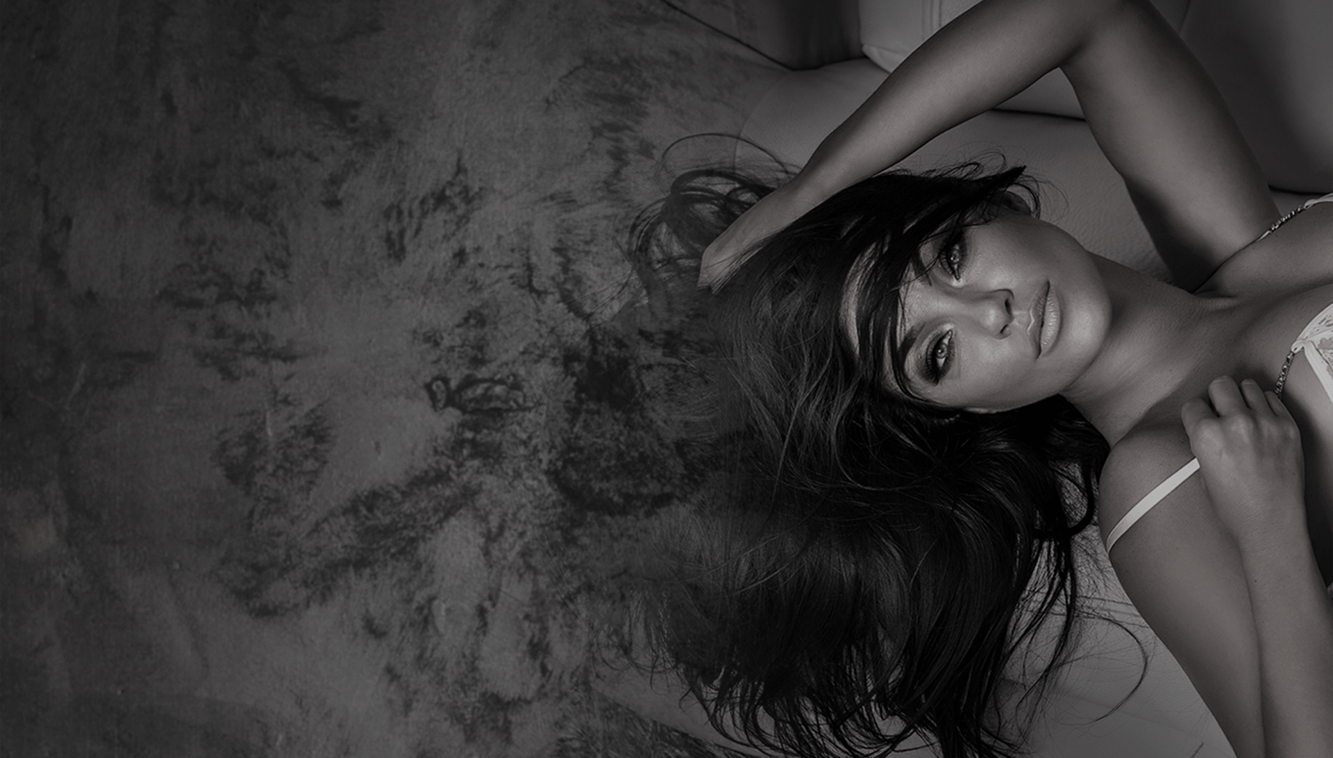 Woman reclining, hair cascading, looking at the viewer. Soft lighting, neutral background.