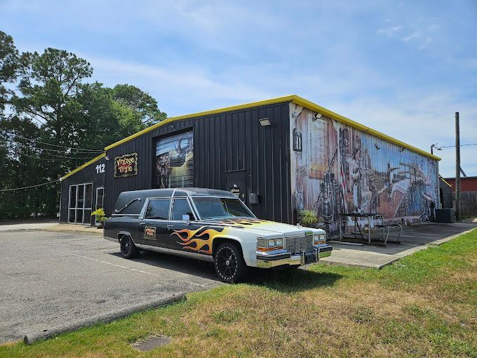 Classic black station wagon parked outside a graffiti-covered industrial building under a blue sky.