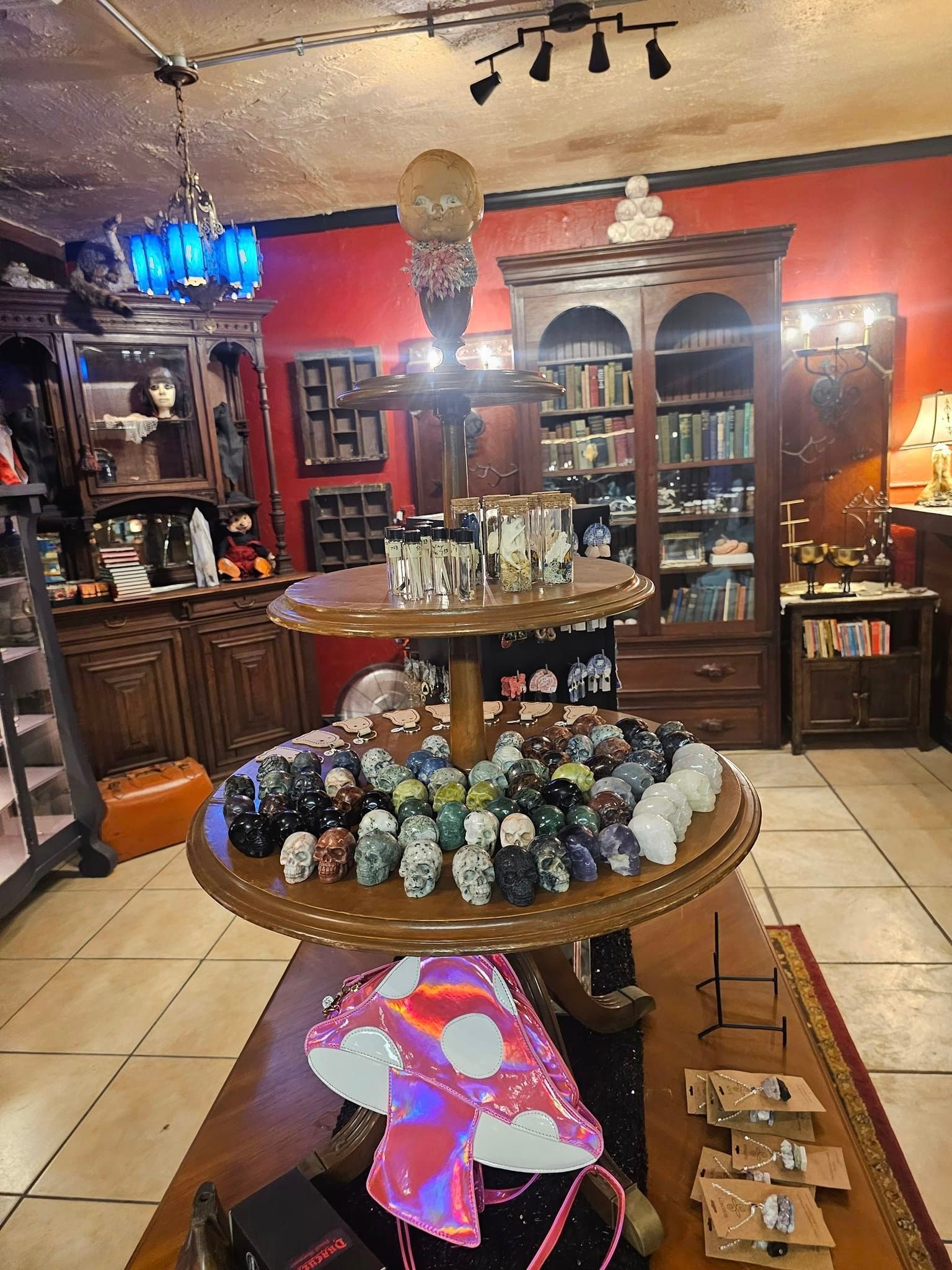 Curio shop with crystal and stone displays on a round table, red walls, cabinets, and hanging lights.