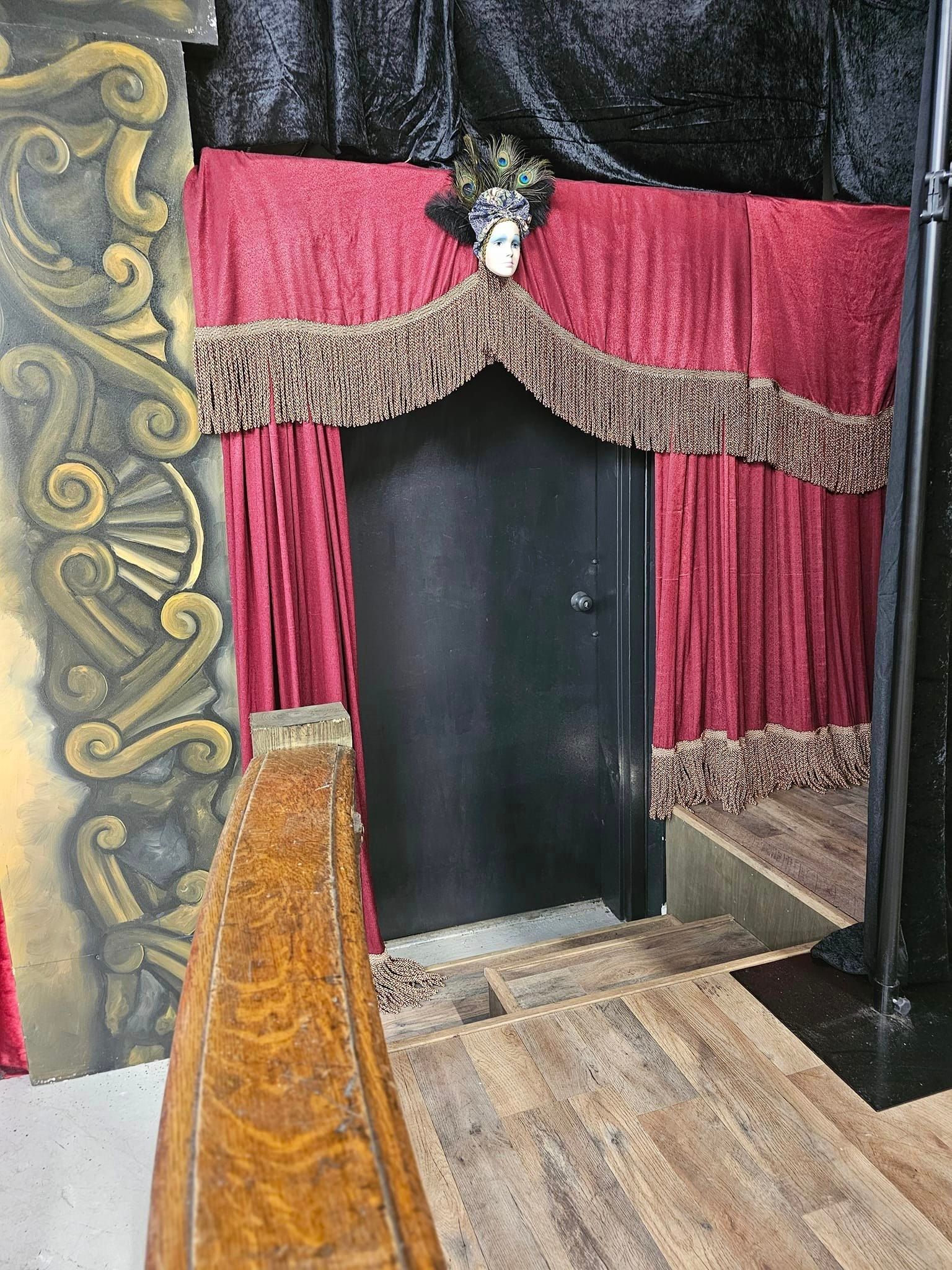 Small theater stage with red curtains, ornate trim, and a black doorway opening at center.