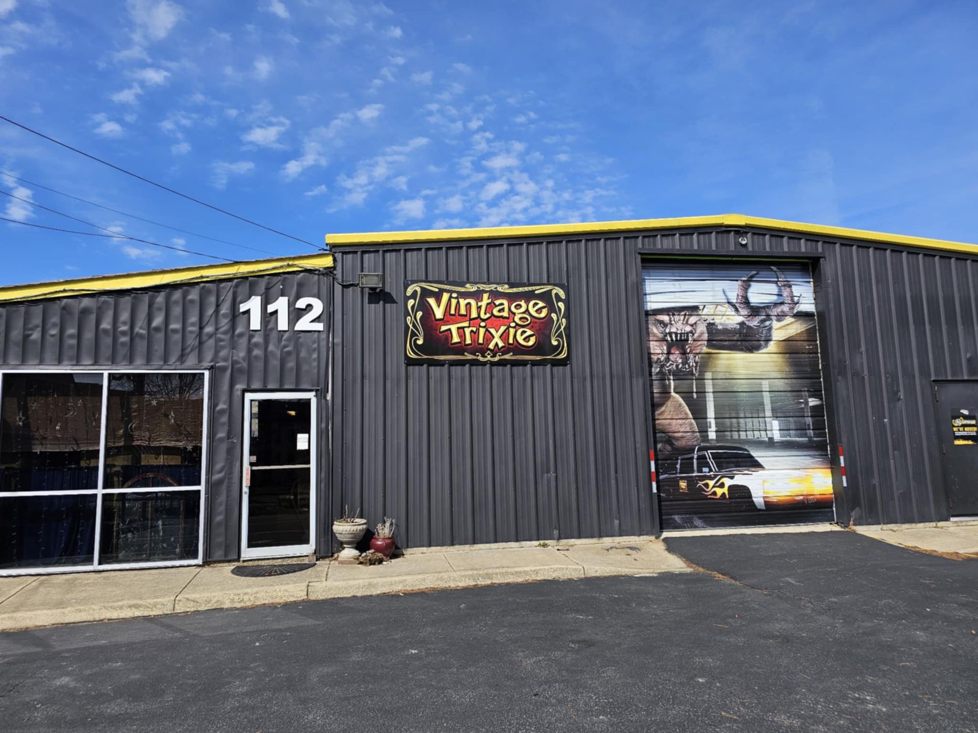 Vintage Vinyl storefront with black siding, large windows, and sign at 112 under a blue sky