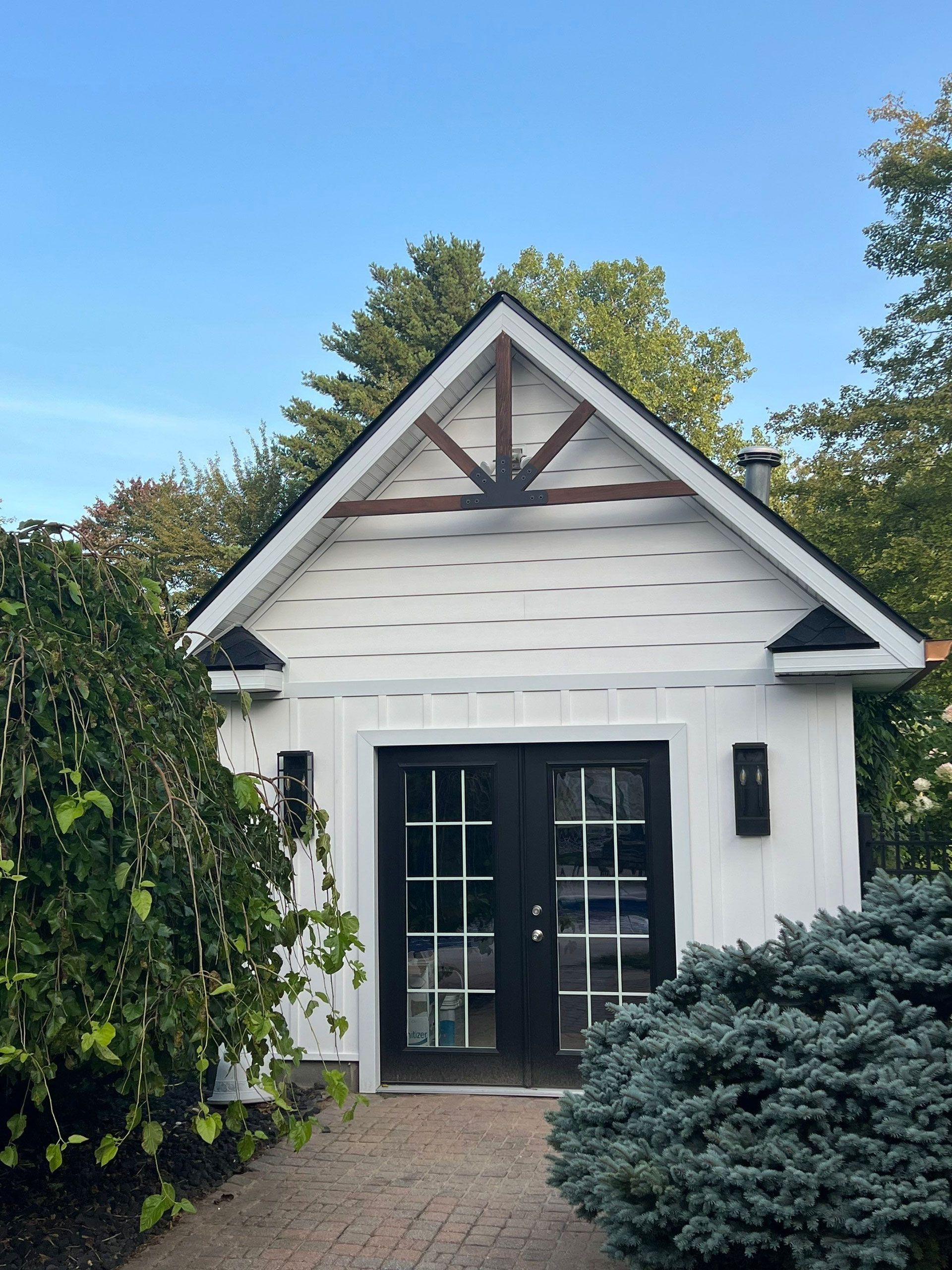 A small white house with a black door is surrounded by trees and bushes