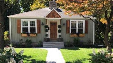 Front view of a small house with white siding, brown shutters, and a landscaped front yard, labeled “AFTER”