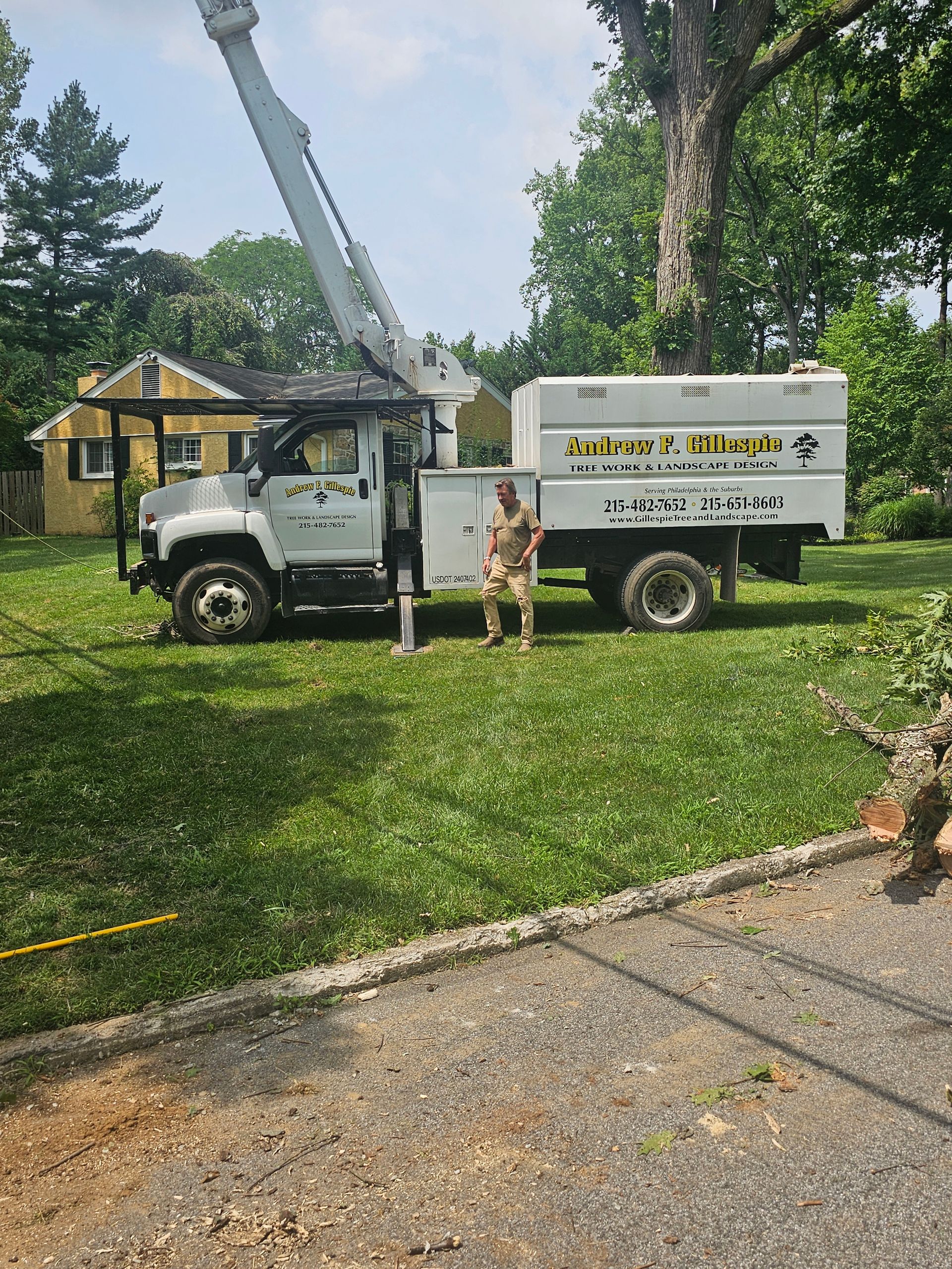 White utility truck and worker beside a house, with a crane and green lawn in the background.
