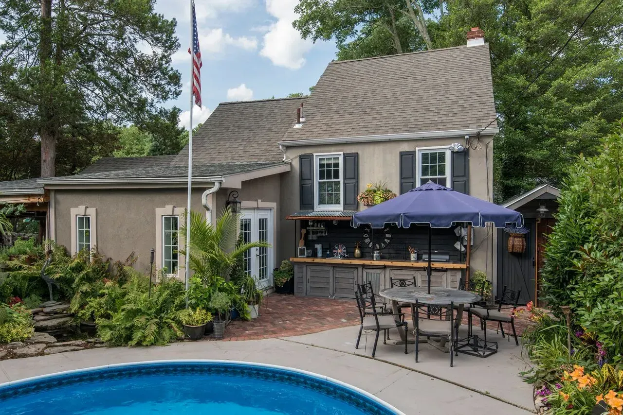 Backyard patio with pool, umbrella table, and a house with landscaped garden