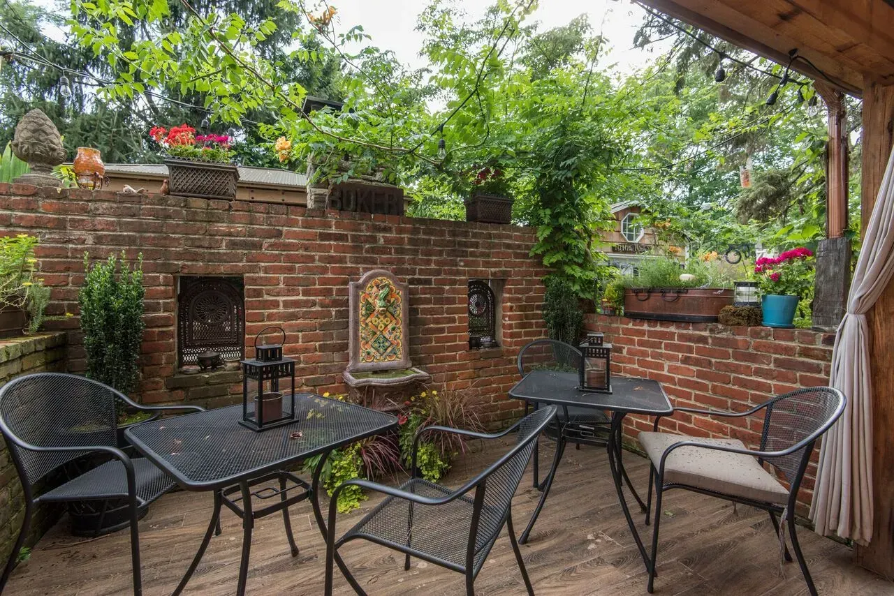 Brick patio with black chairs and table in a leafy garden courtyard