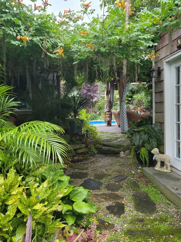 Lush tropical garden path with stone steps, palm leaves, and a small blue pool in the background