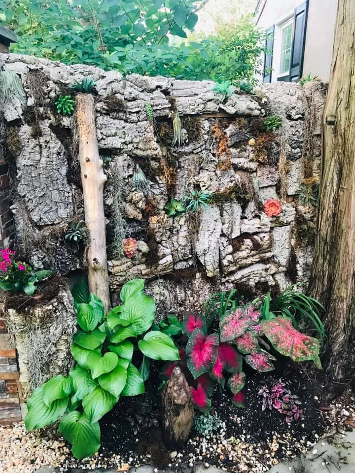 Rustic stone wall with lush green and pink flowering plants in a garden corner