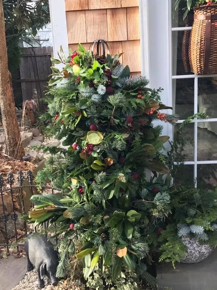 Decorated outdoor topiary with greenery, ornaments, and flowers beside a house window