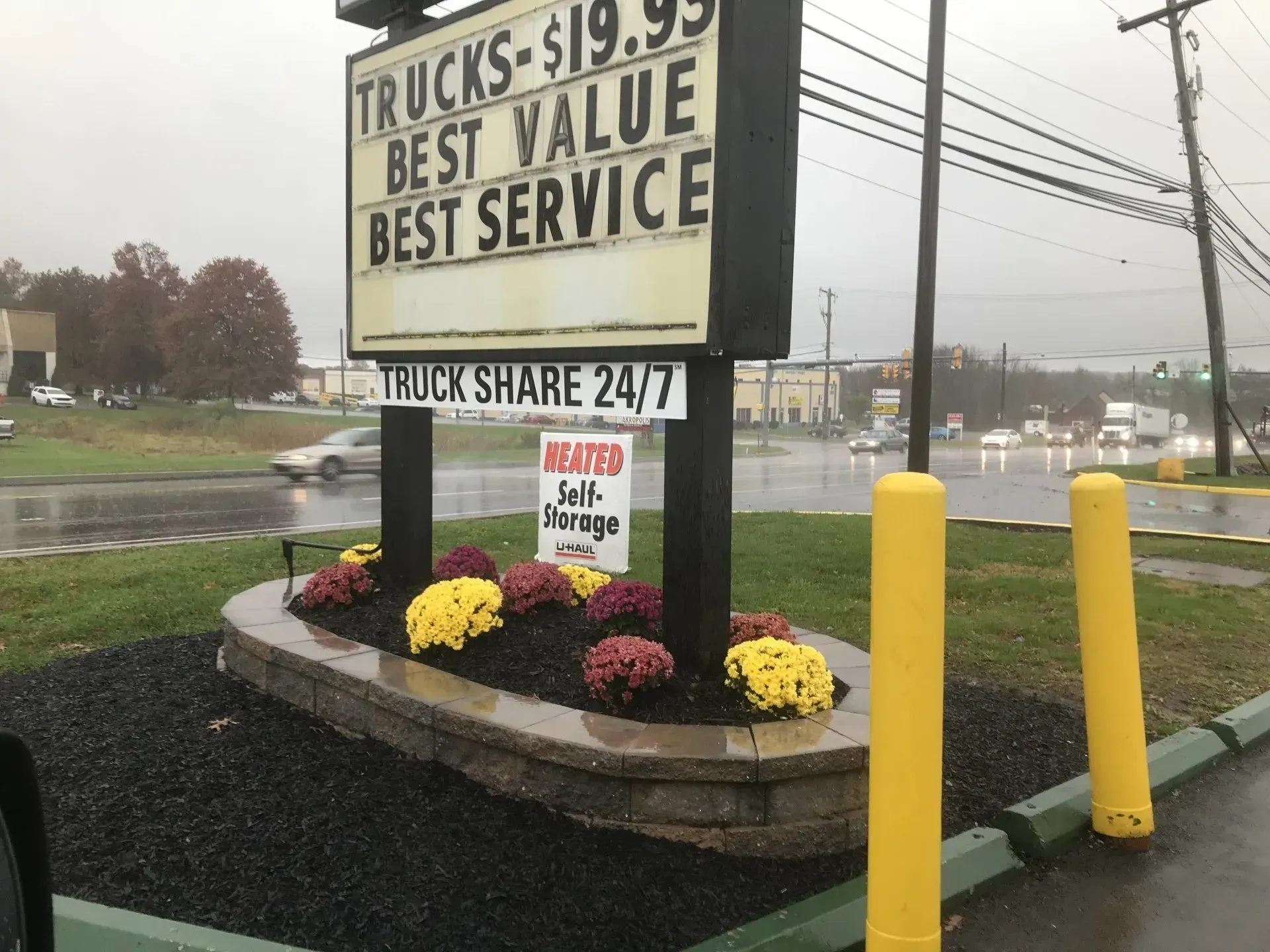 Sign for best value truck service beside a roadside with flowers and yellow safety posts