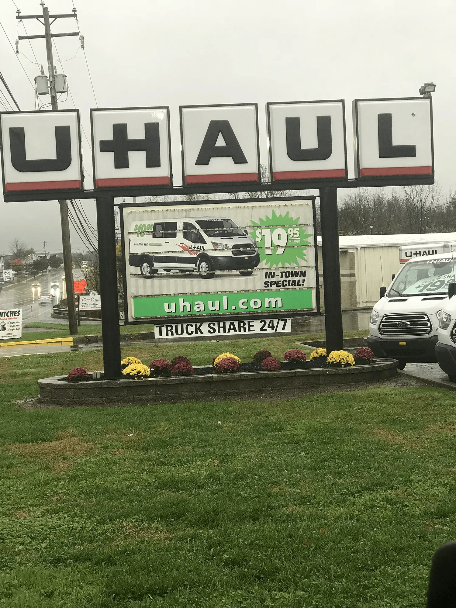 U-Haul storefront sign beside a roadside lot with a green moving-truck banner and parked trucks on a cloudy day