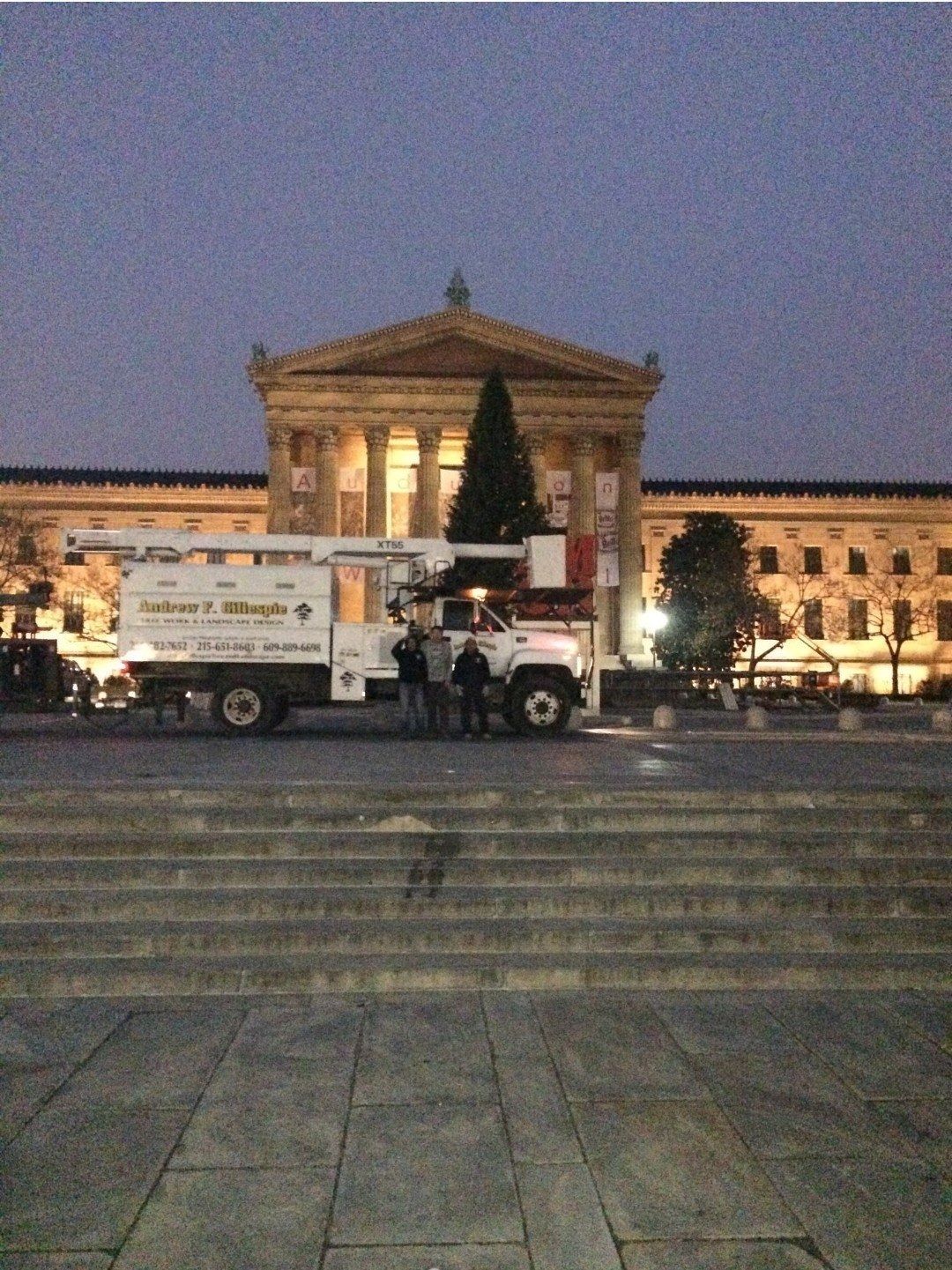 Work truck with a lit Christmas tree in front of a grand building at dusk