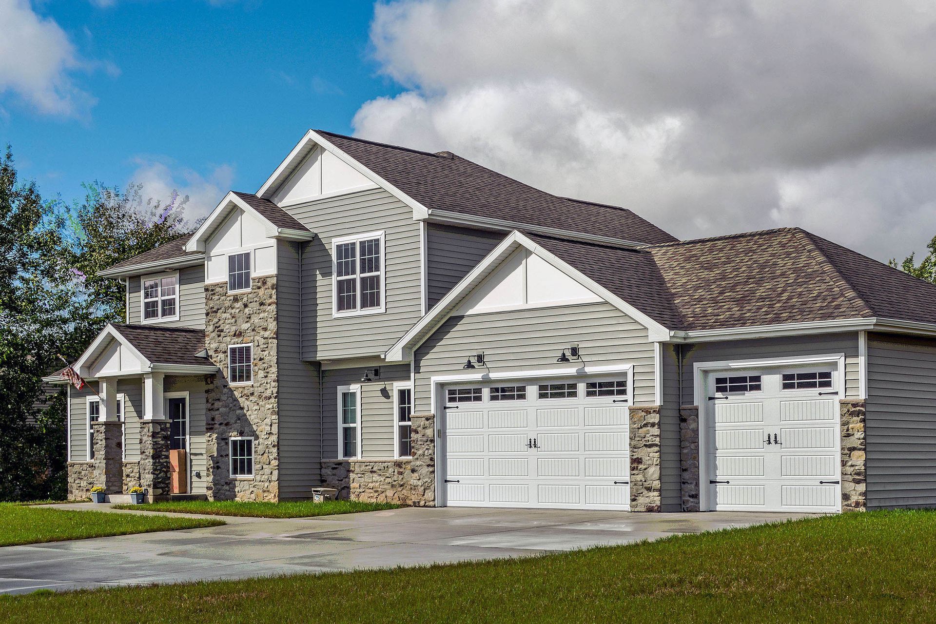 Two-story gray house with stone accents, white trim, and a two-car garage on a sunny day.