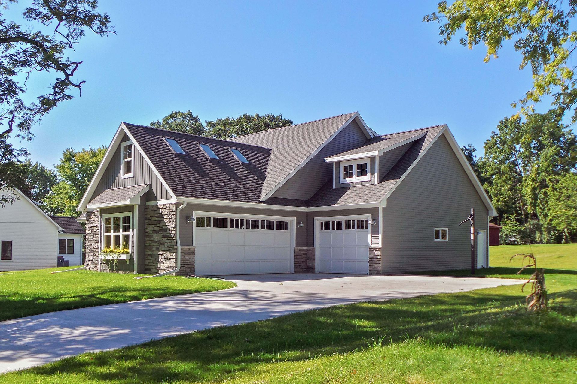 Gray two-car garage with white doors, stone accents, and two dormers under a clear blue sky.