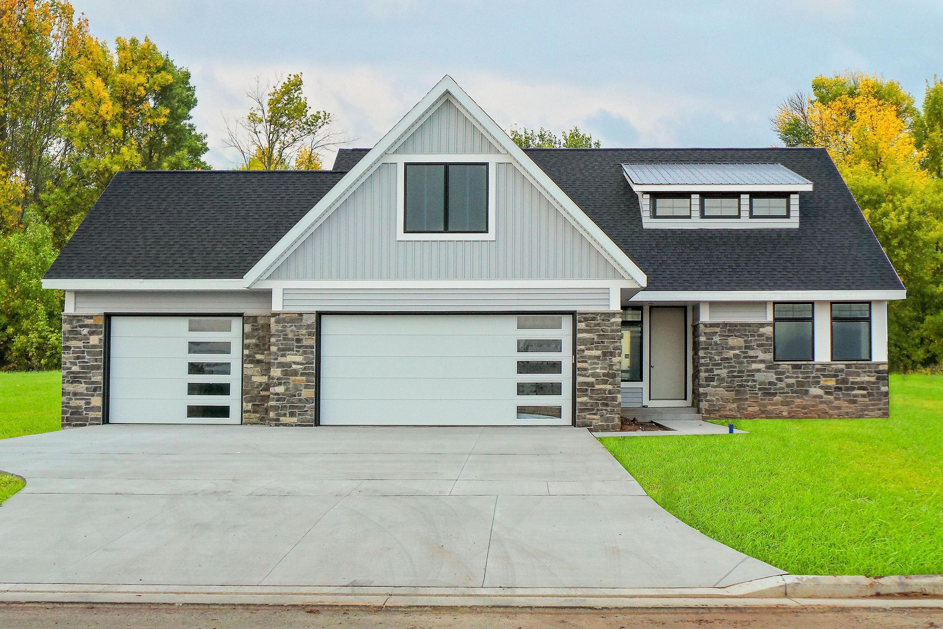 Modern house with light gray siding, stone accents, black roof, and two garage doors.