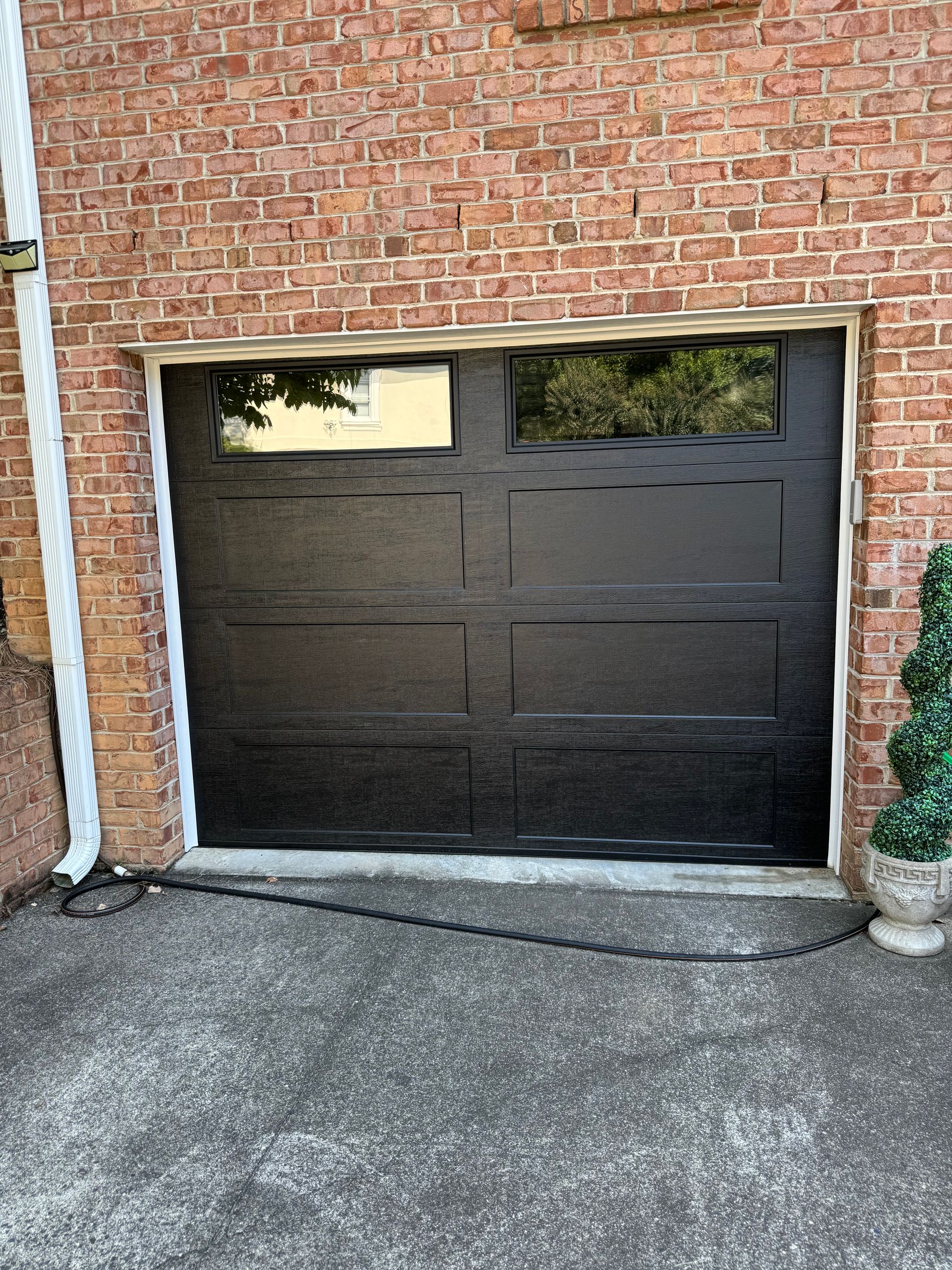 Black garage door with two window panels set in a red brick building, in a paved driveway.