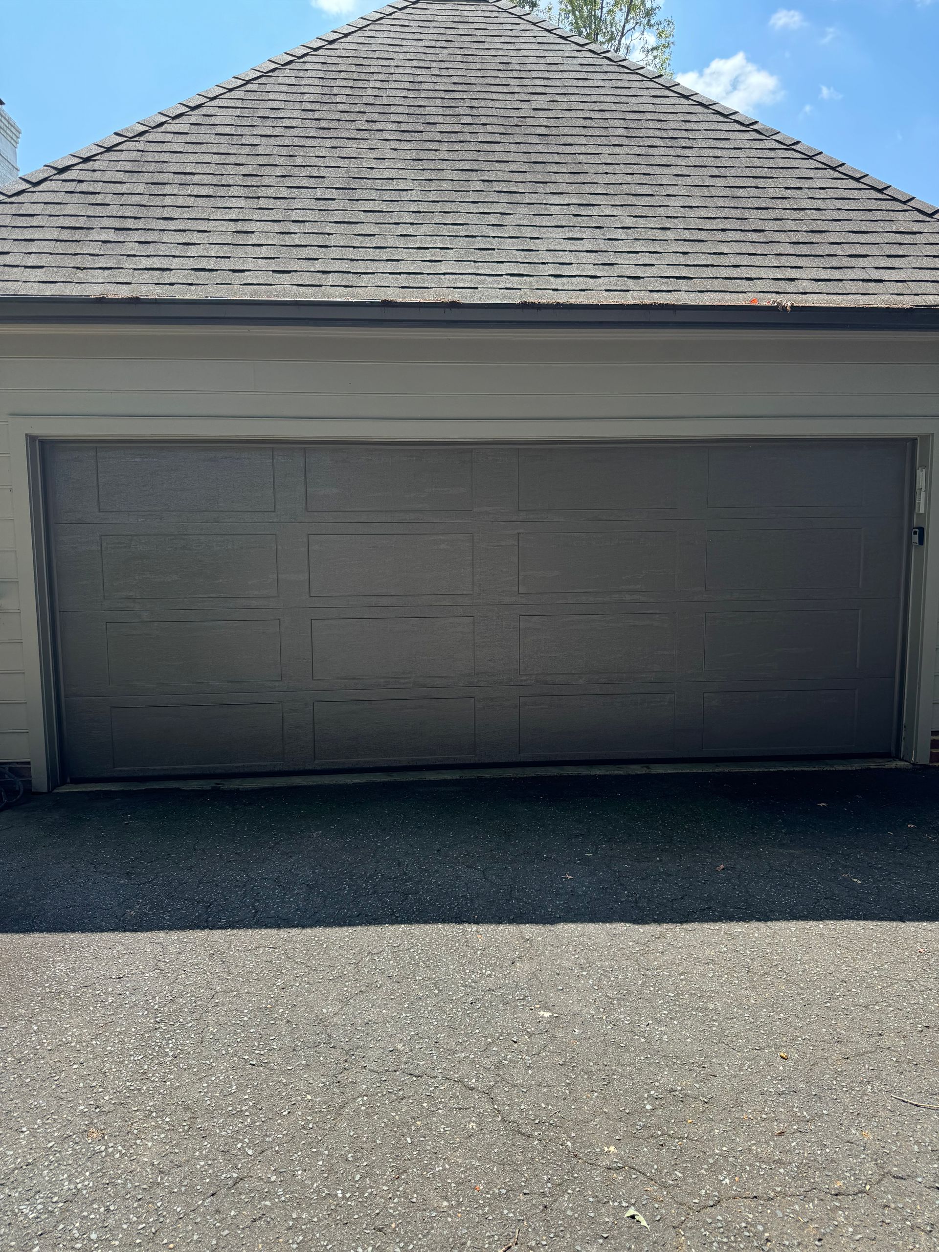 Gray garage door under a gray roof on a sunny day.