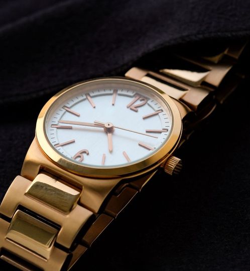A gold watch with a white face and roman numerals