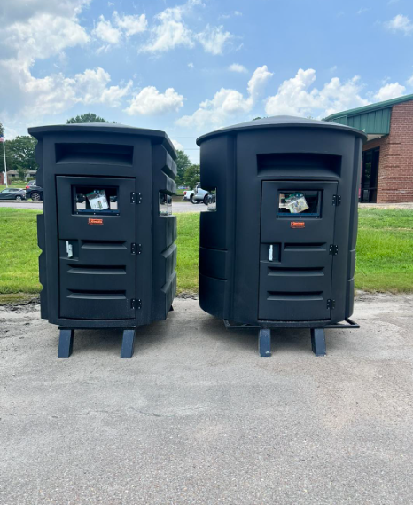 Two black trash cans are sitting next to each other in a parking lot