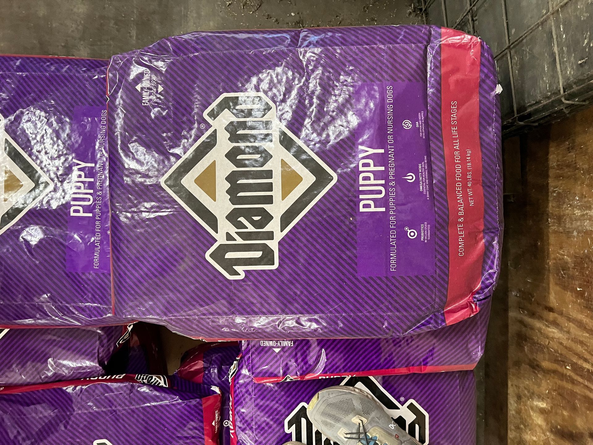A bag of Diamond puppy dog food is sitting on top of a pile of other bags.