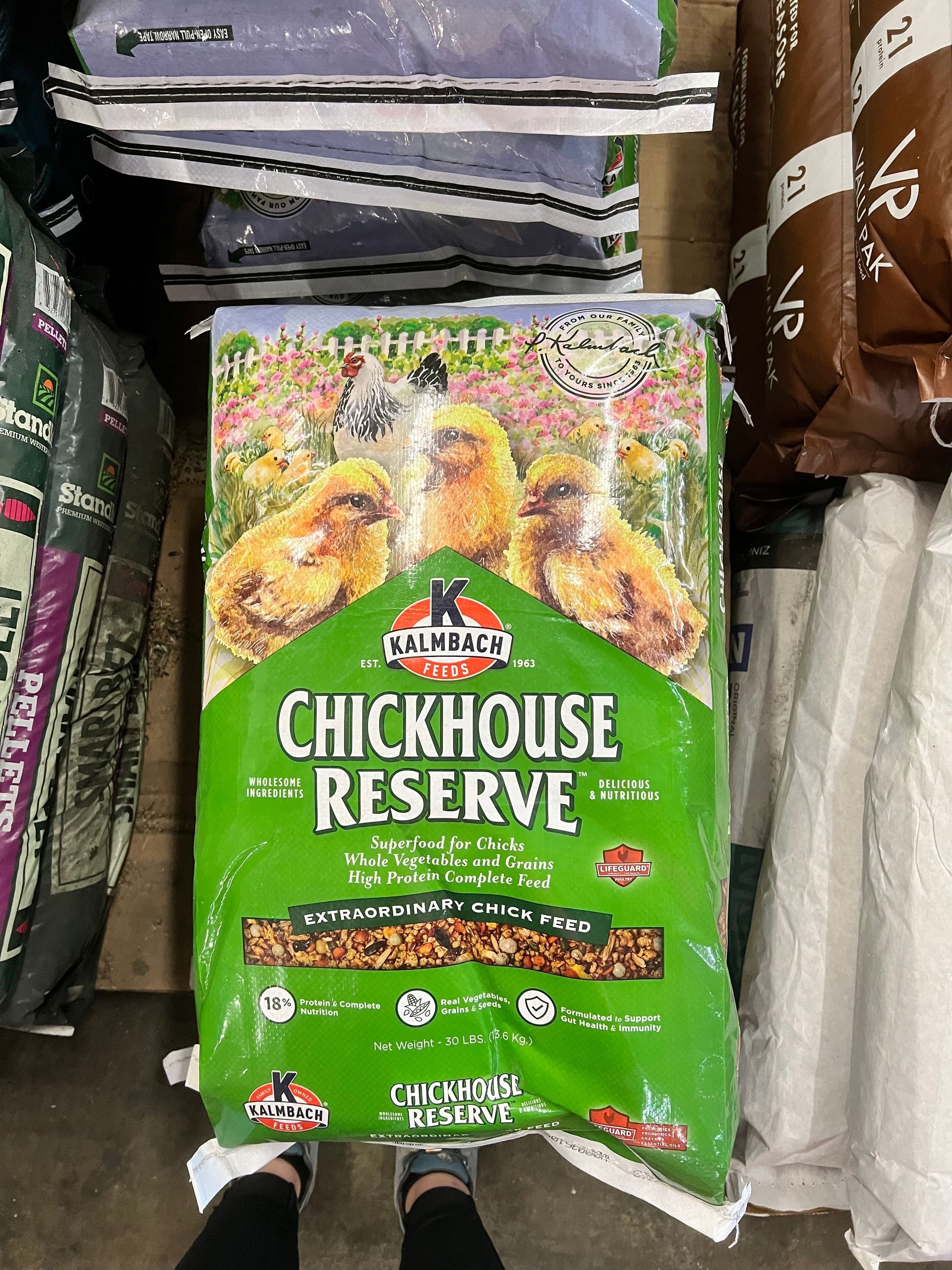A person is standing next to a bag of chickhouse reserve chicken food.