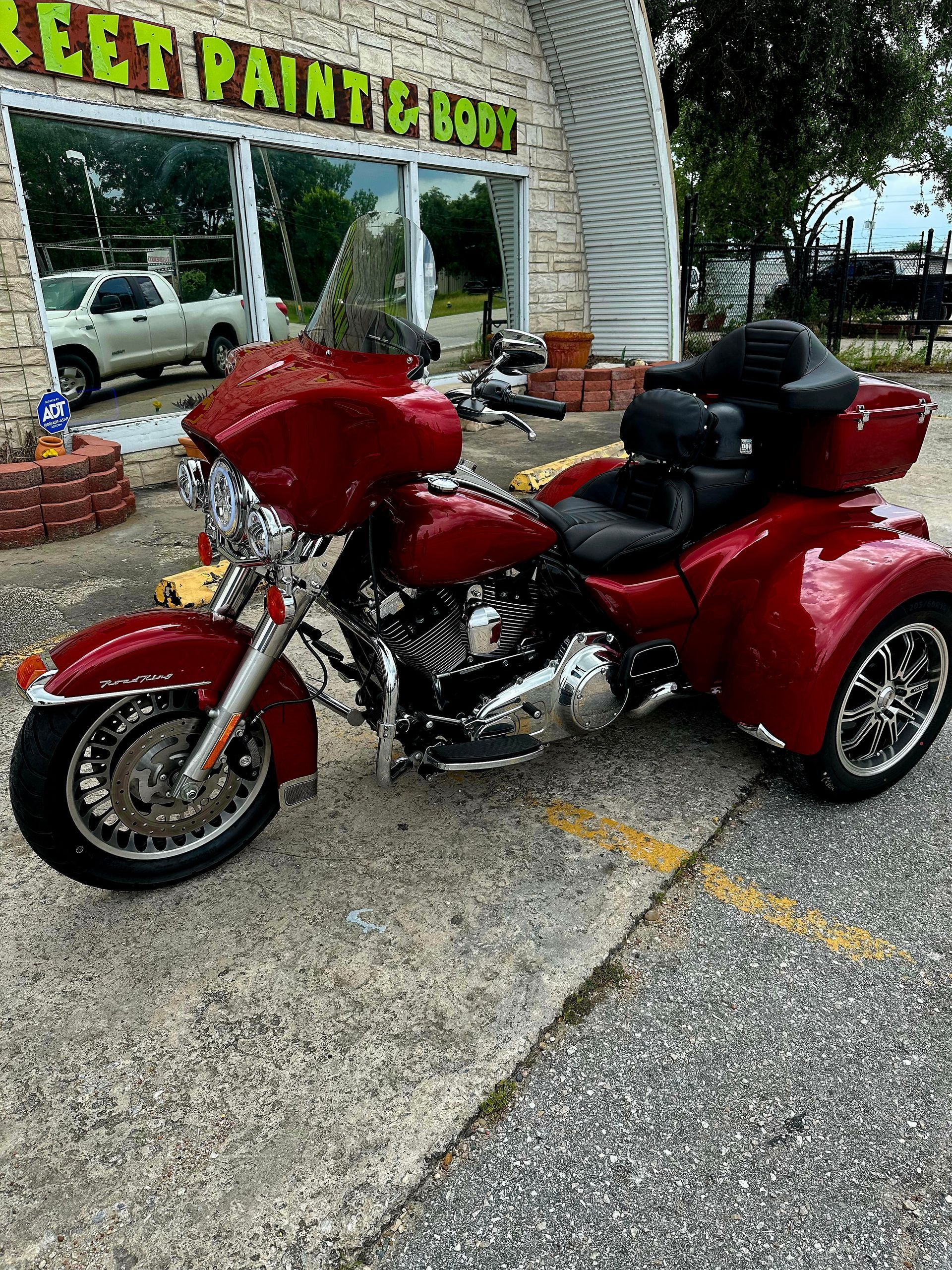 A red motorcycle with three wheels is parked in front of a building.