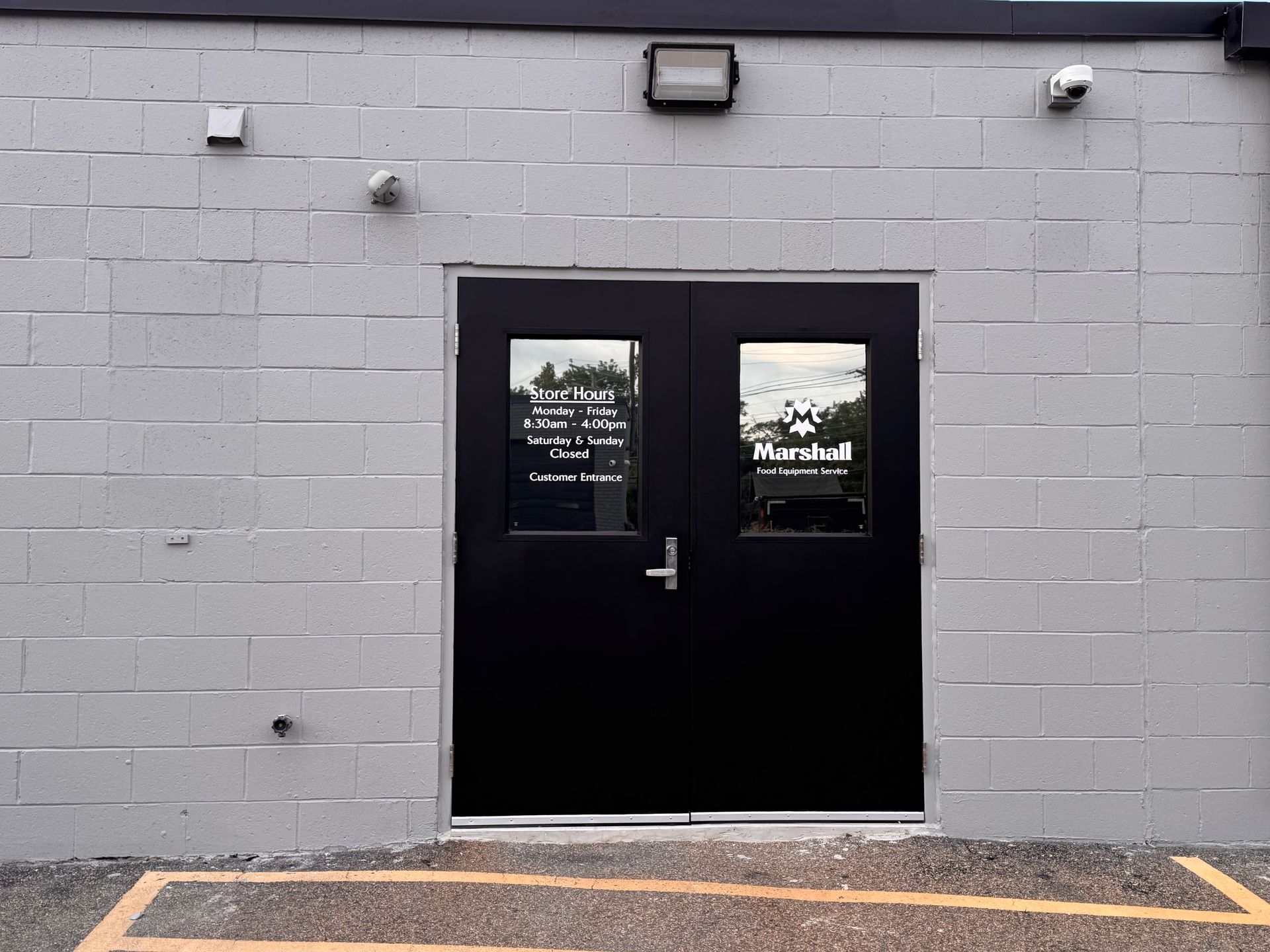 Black double doors with windows, gray block building, security cameras, yellow curb paint.