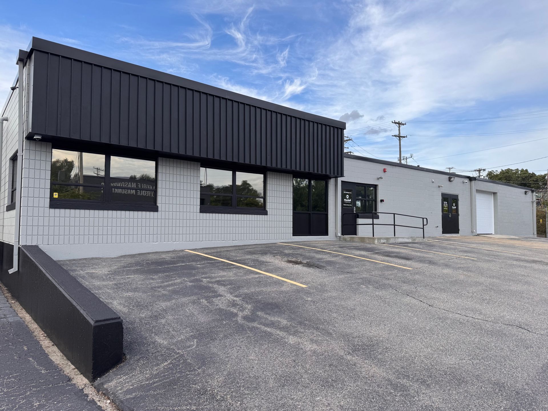 Gray commercial building with black accents, fronted by a ramp and parking area.