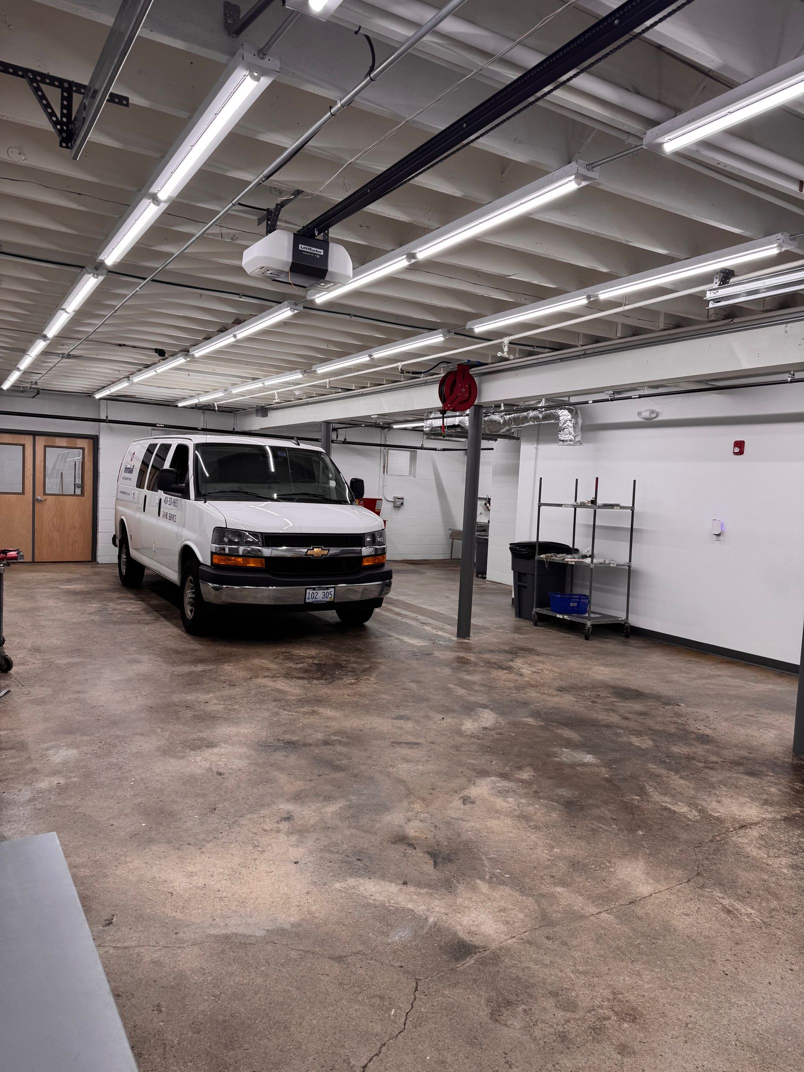 White van parked inside a brightly lit garage with overhead lights.