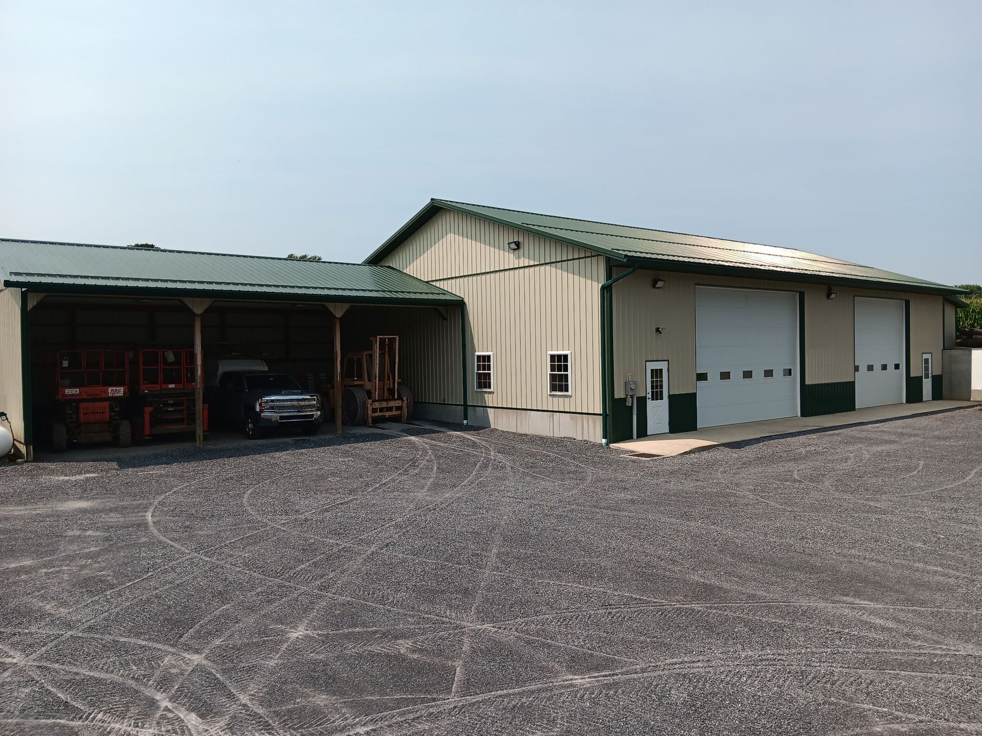 Two metal warehouses with open bays and closed garage doors on a gravel lot.