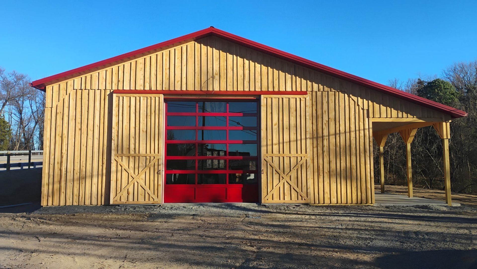 Yellow wooden barn with red roof and red sliding doors under a clear blue sky.