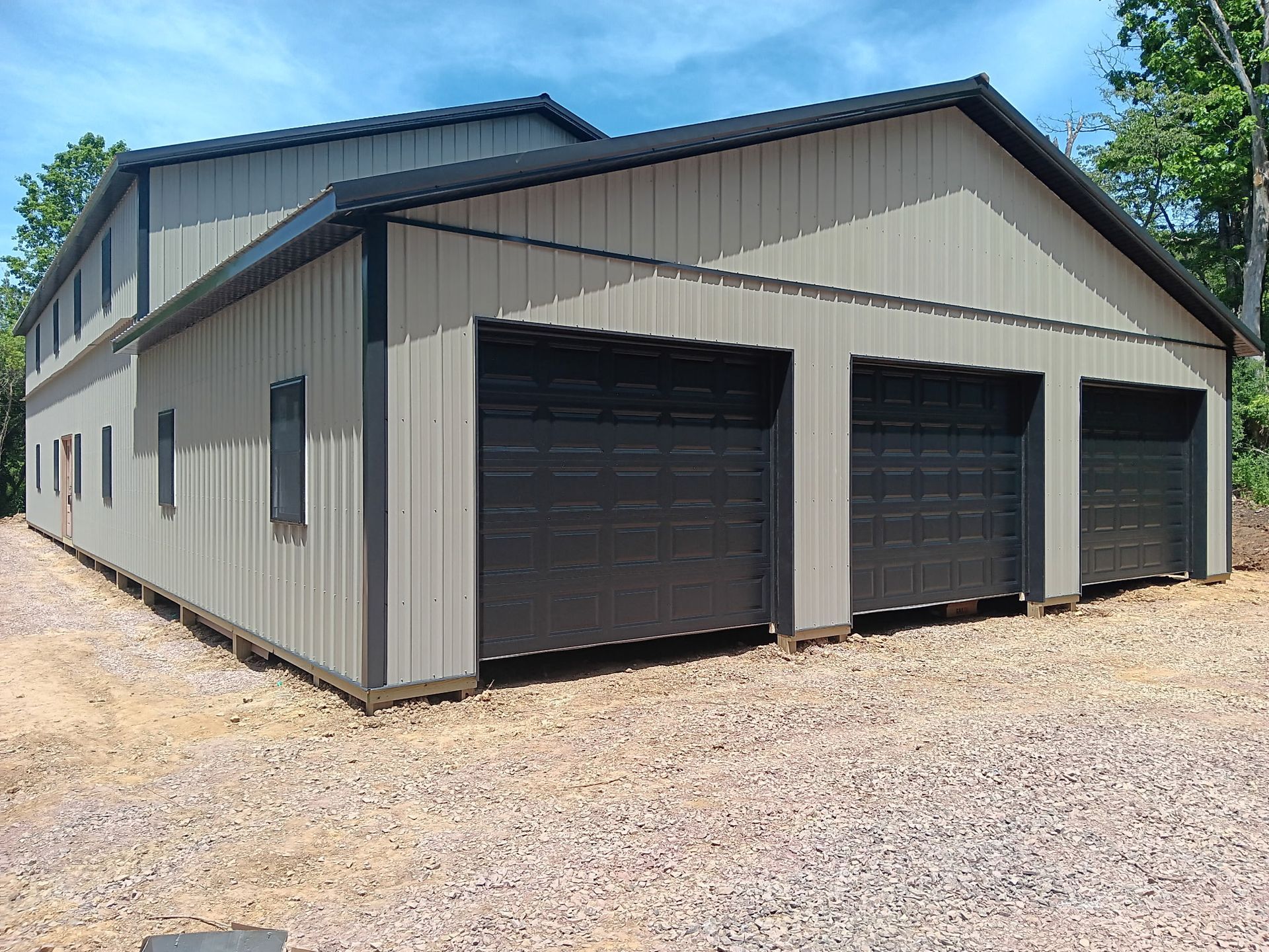 Large gray metal storage building with three dark garage doors on a gravel lot
