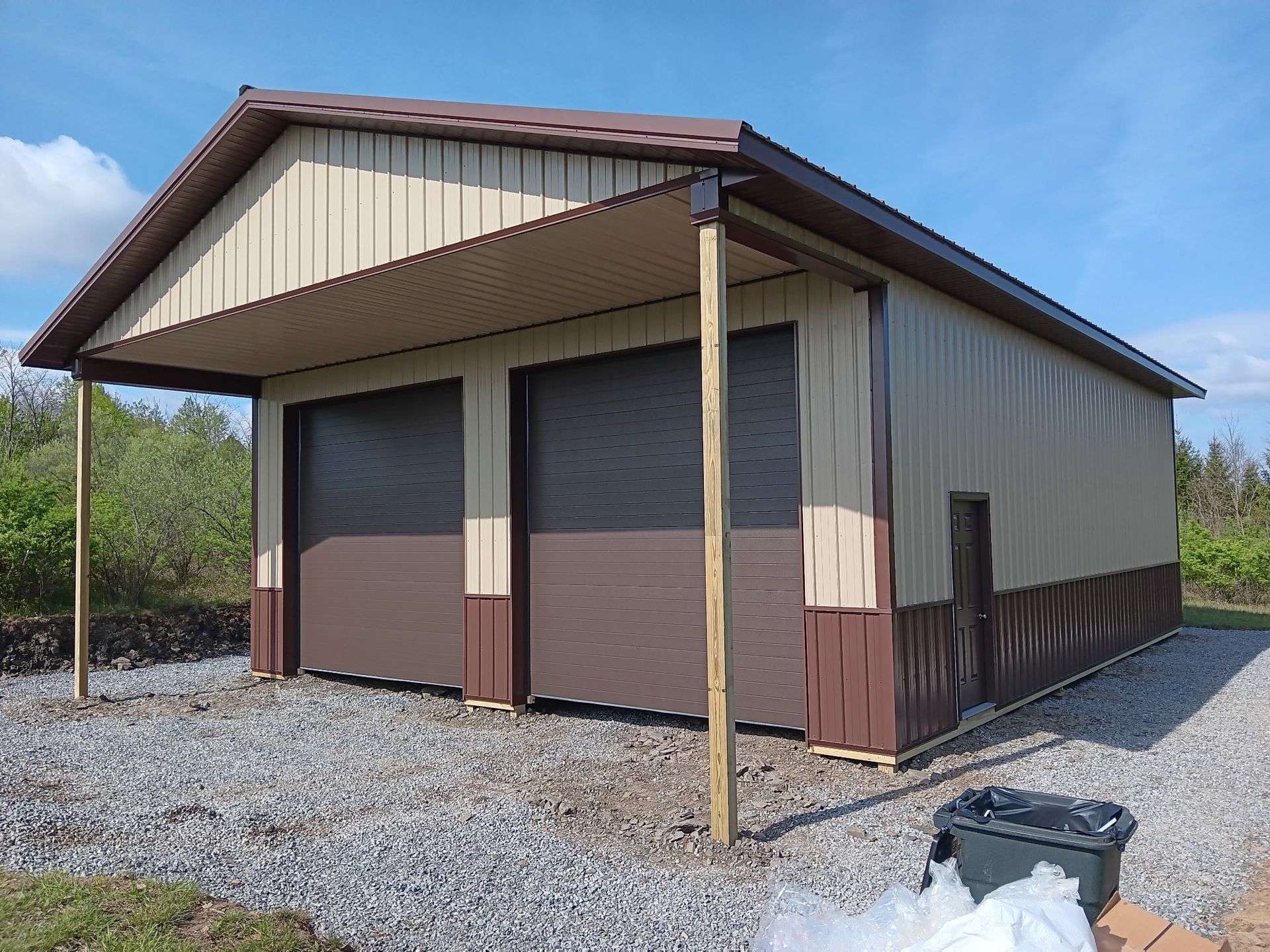 Small metal storage building with tan siding and brown trim on a gravel lot under a blue sky