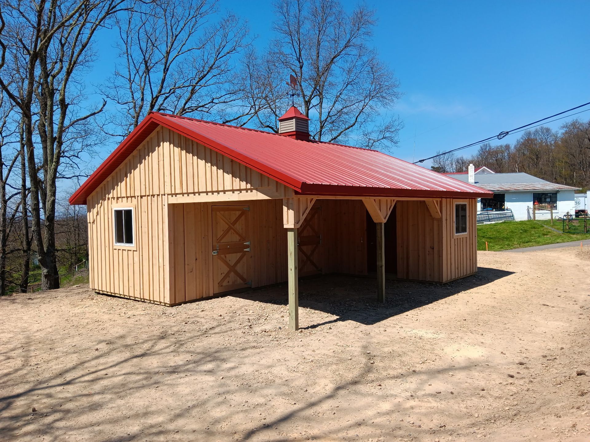 Small tan wooden shed with a red metal roof on sandy ground under a clear blue sky