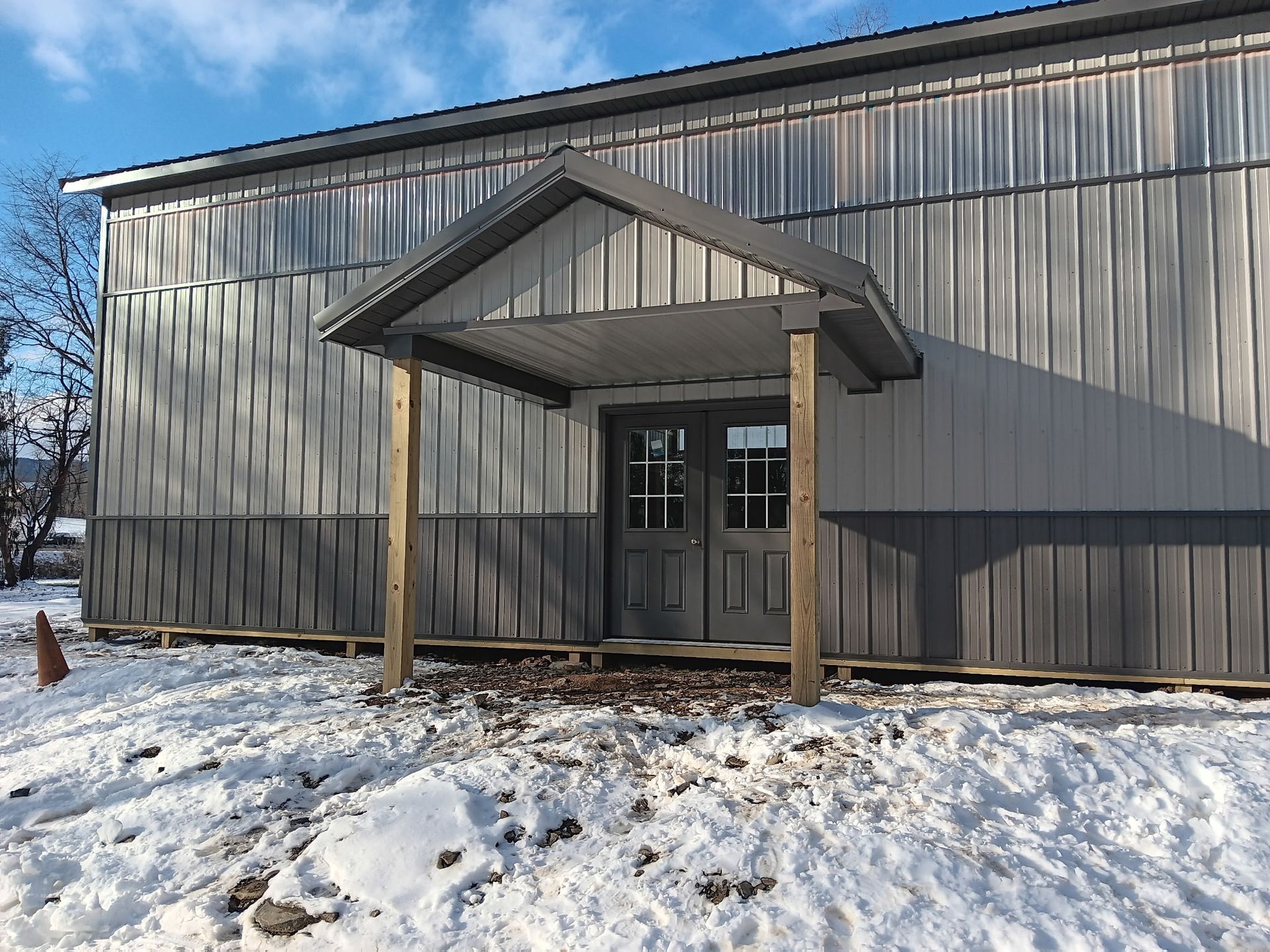 Snow-covered metal building entrance with a small covered porch and double glass doors