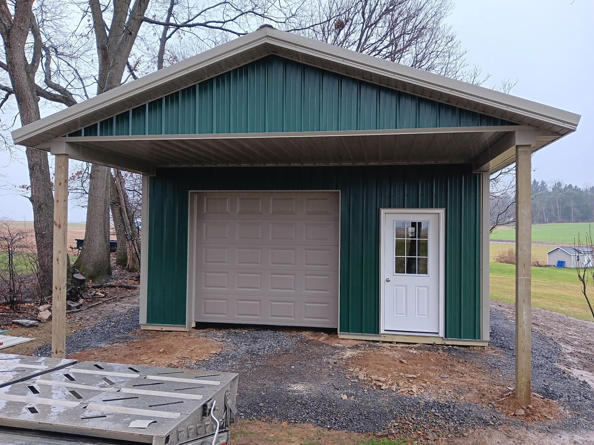 Small teal outbuilding with a beige garage door and white side door in a rural yard.