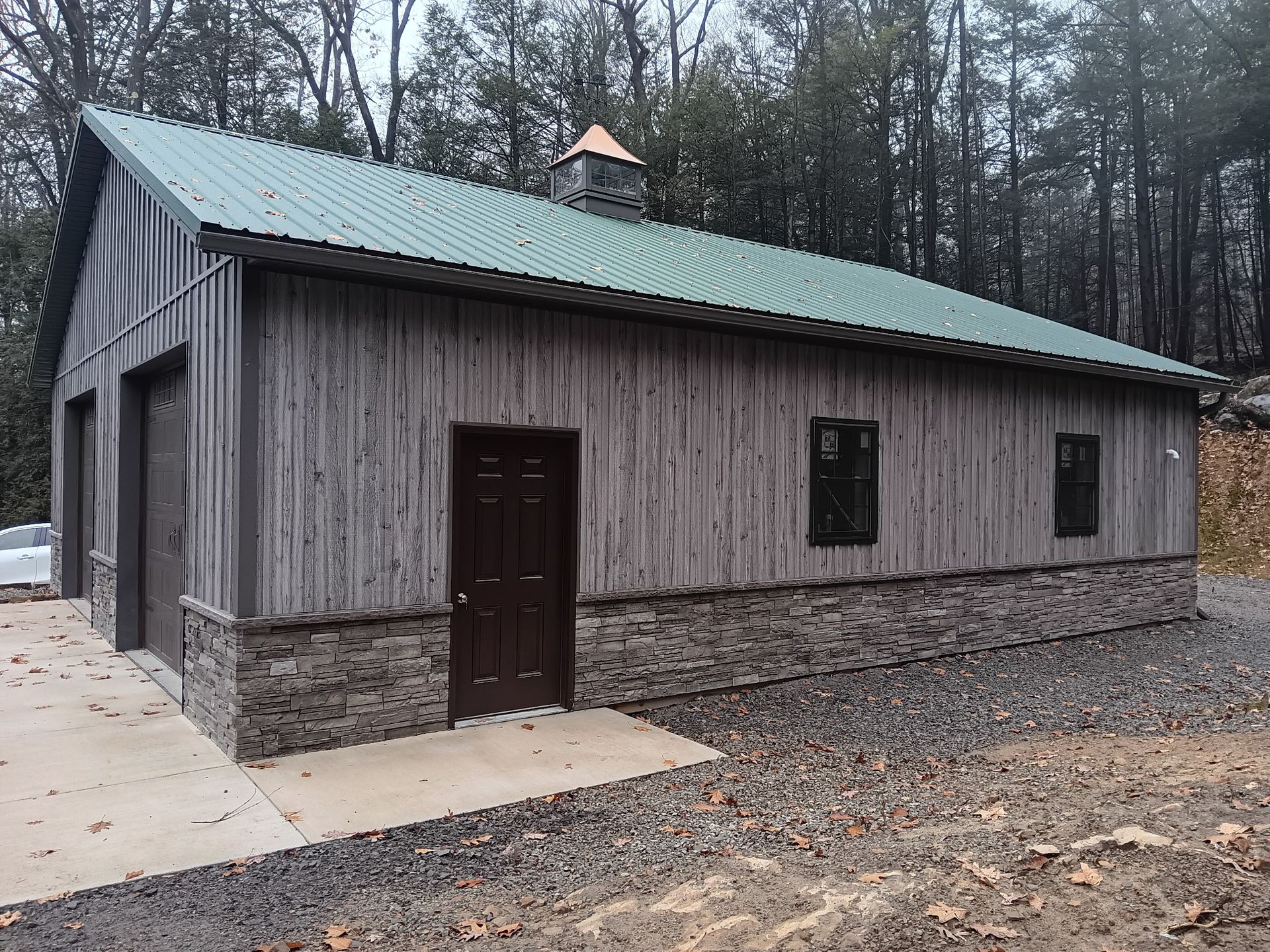 Small rustic cabin with gray wood siding, green metal roof, and a dark door in a wooded setting.