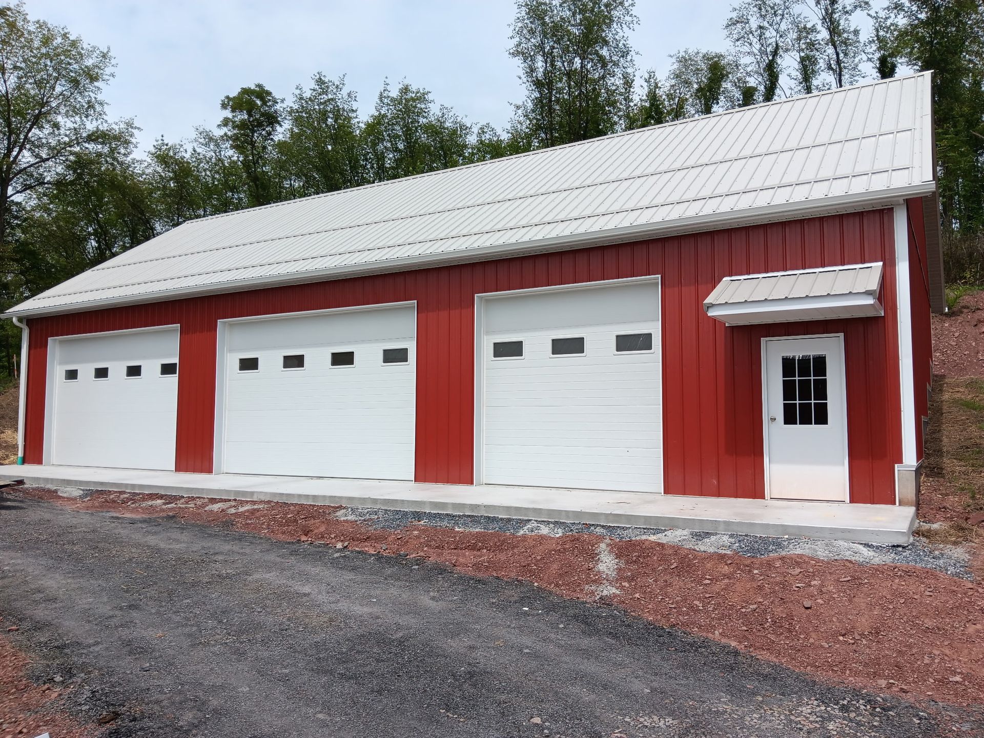 Red barn-style garage with four white overhead doors and a white side entry door on a gravel drive