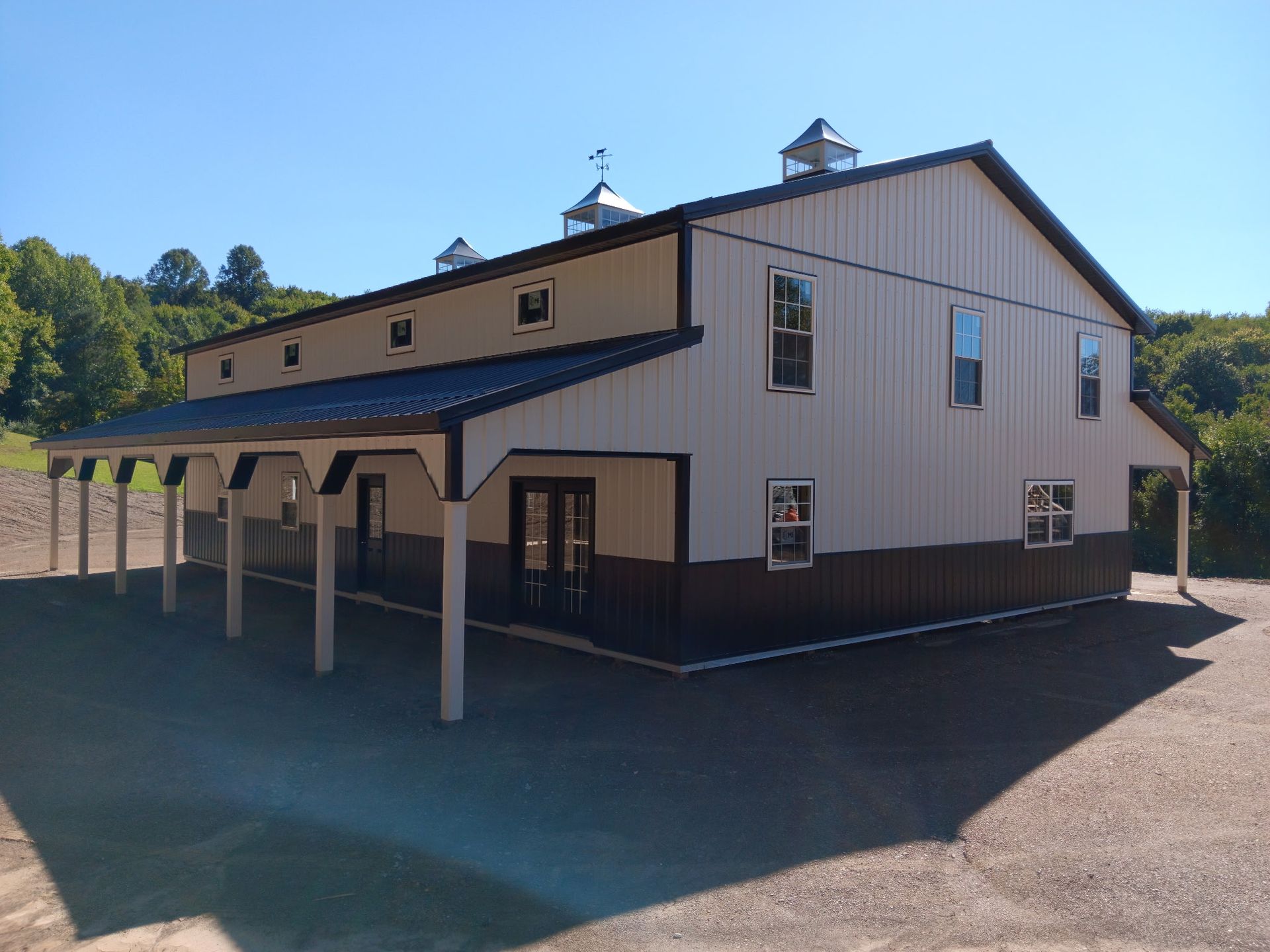 Large beige barn-style building with a covered walkway and cupolas on a sunny day