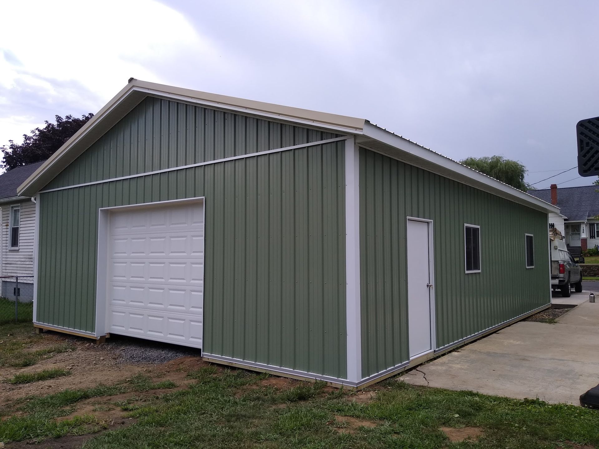 Green metal garage building with white trim, roll-up door, and side entry on a concrete pad
