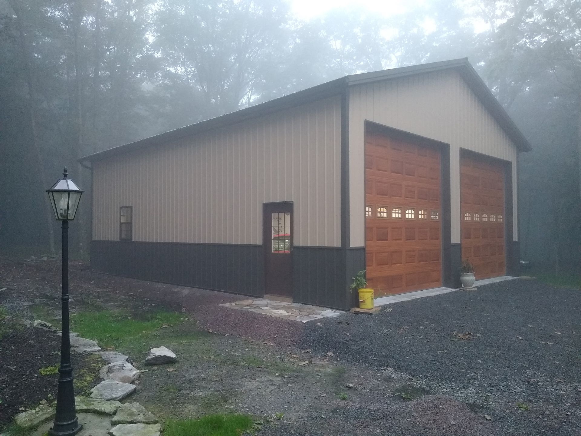 Large beige garage with brown doors and a yellow fire hydrant on a misty gravel driveway