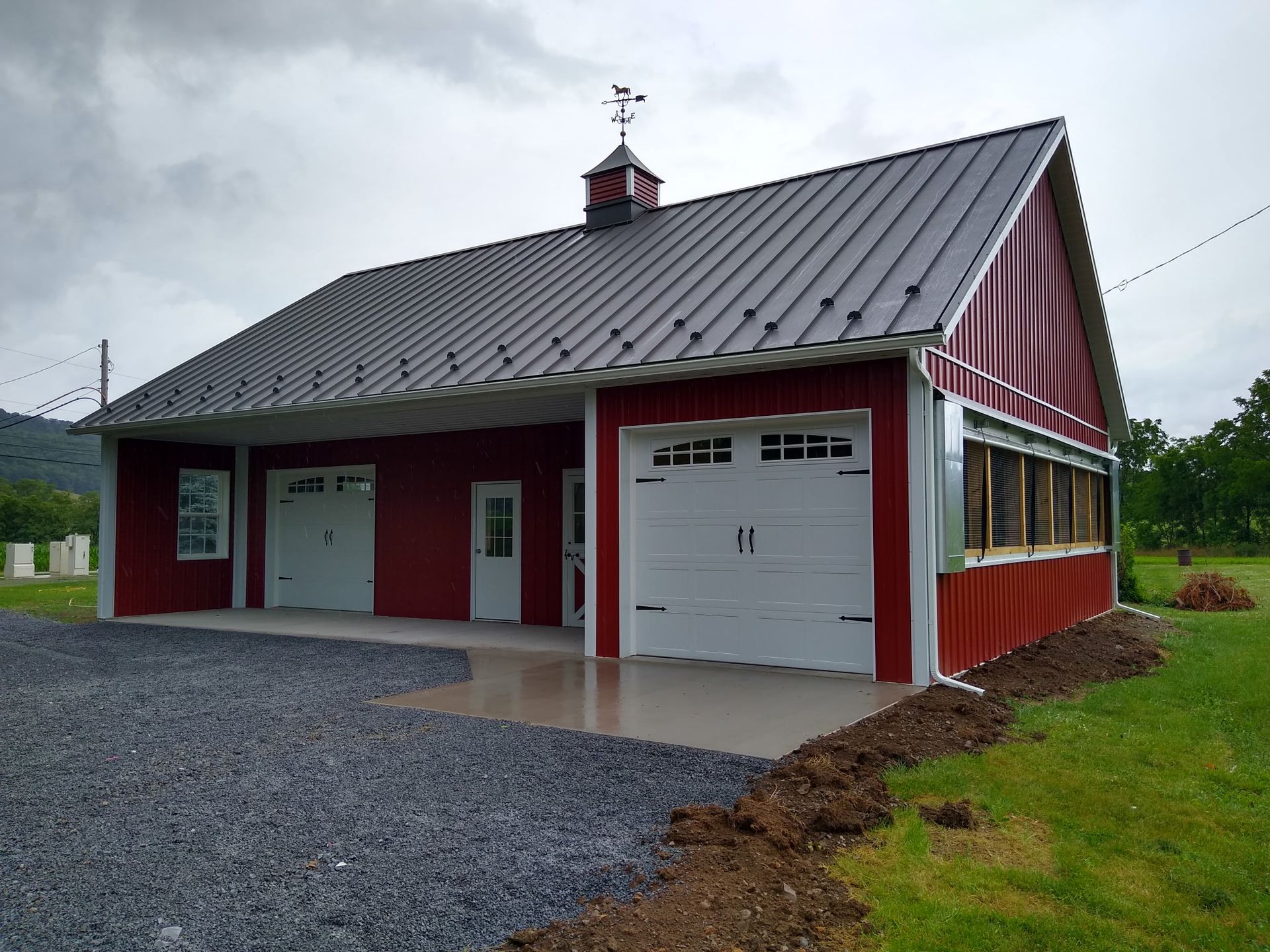 Red barn-style garage with white doors, metal roof, and gravel driveway outdoors