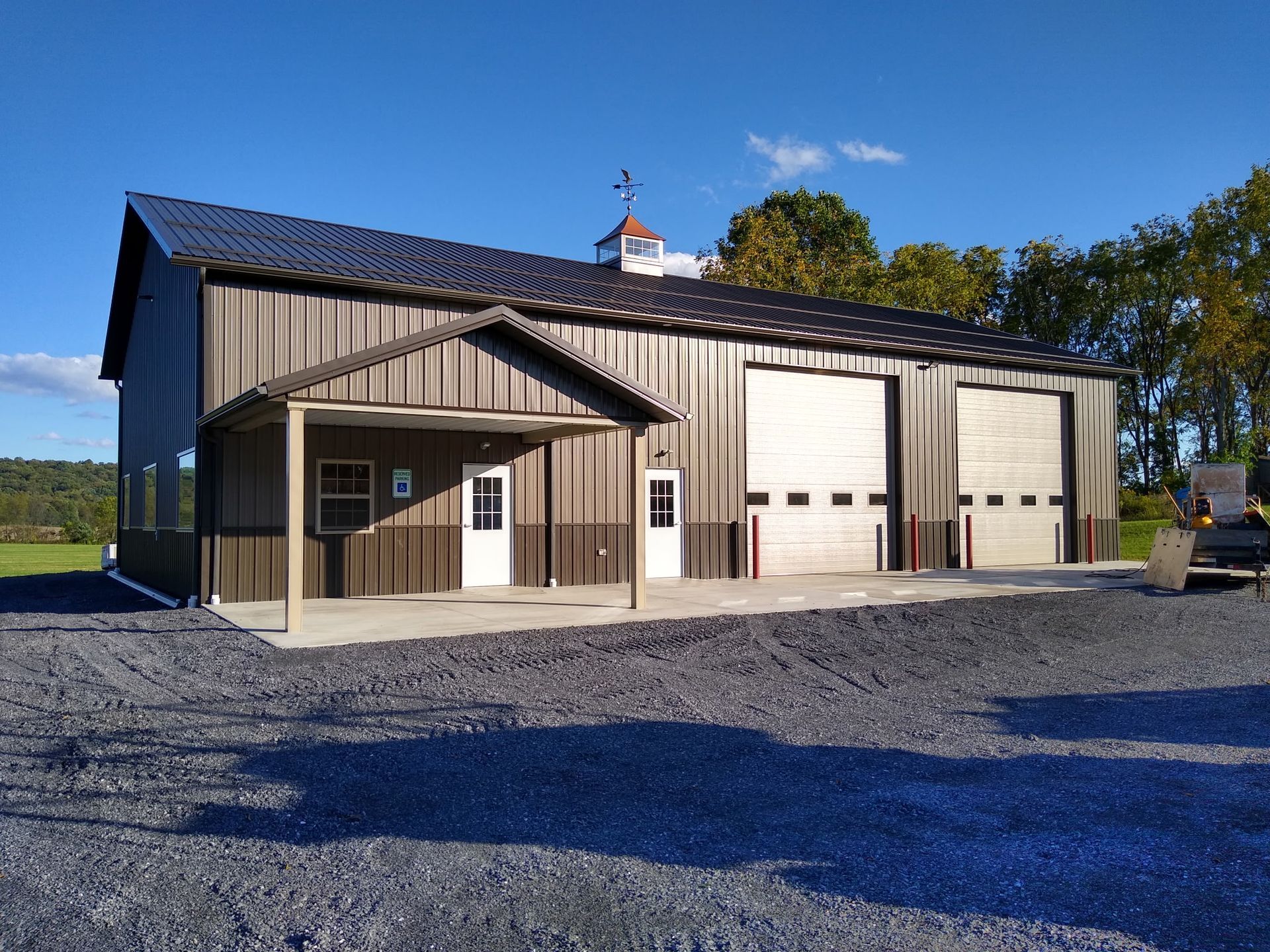 White barn with large garage doors and a small porch on a gravel lot under a clear blue sky.