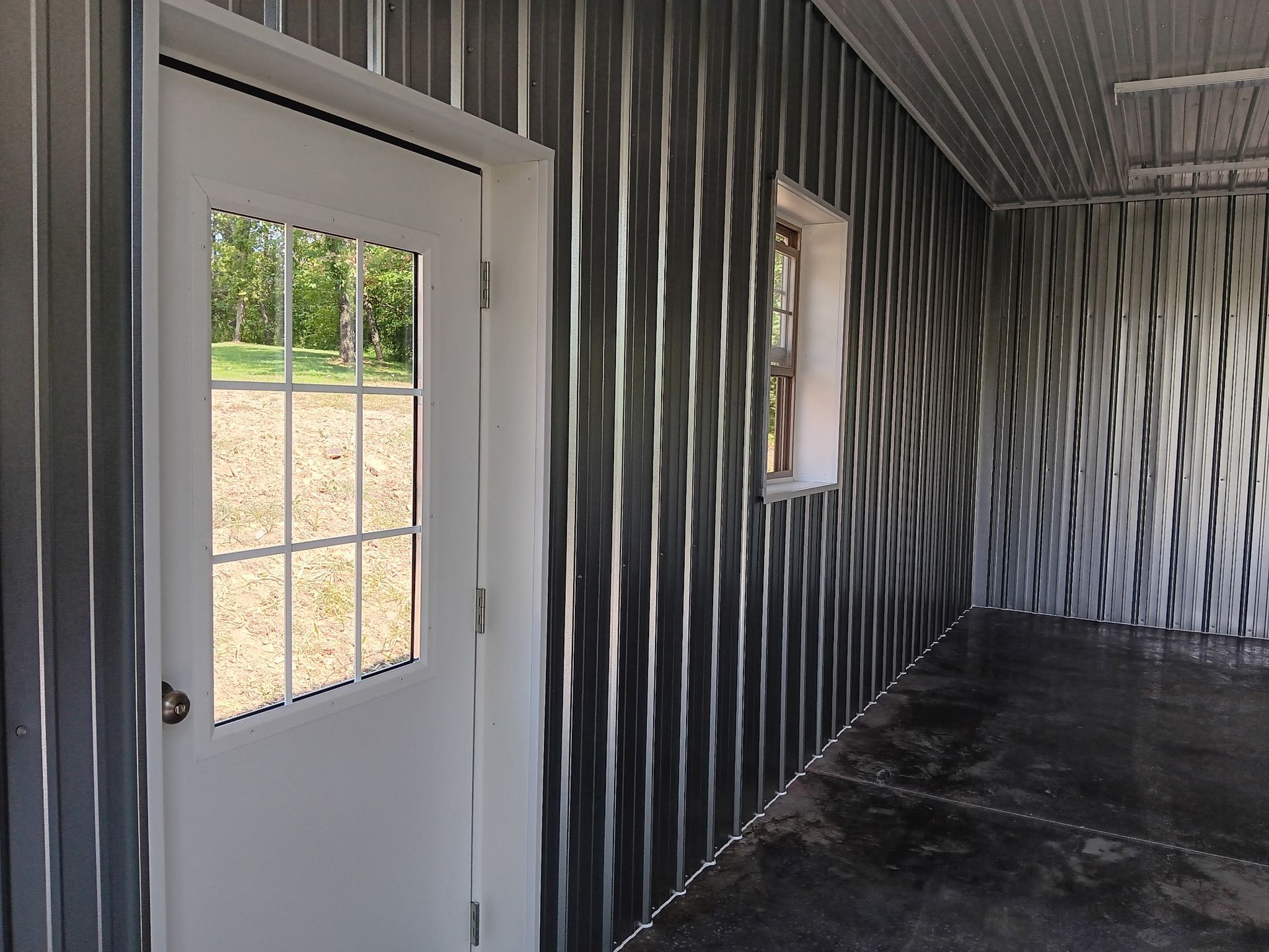 Covered porch with a white door, striped wall paneling, and a small window overlooking outdoors