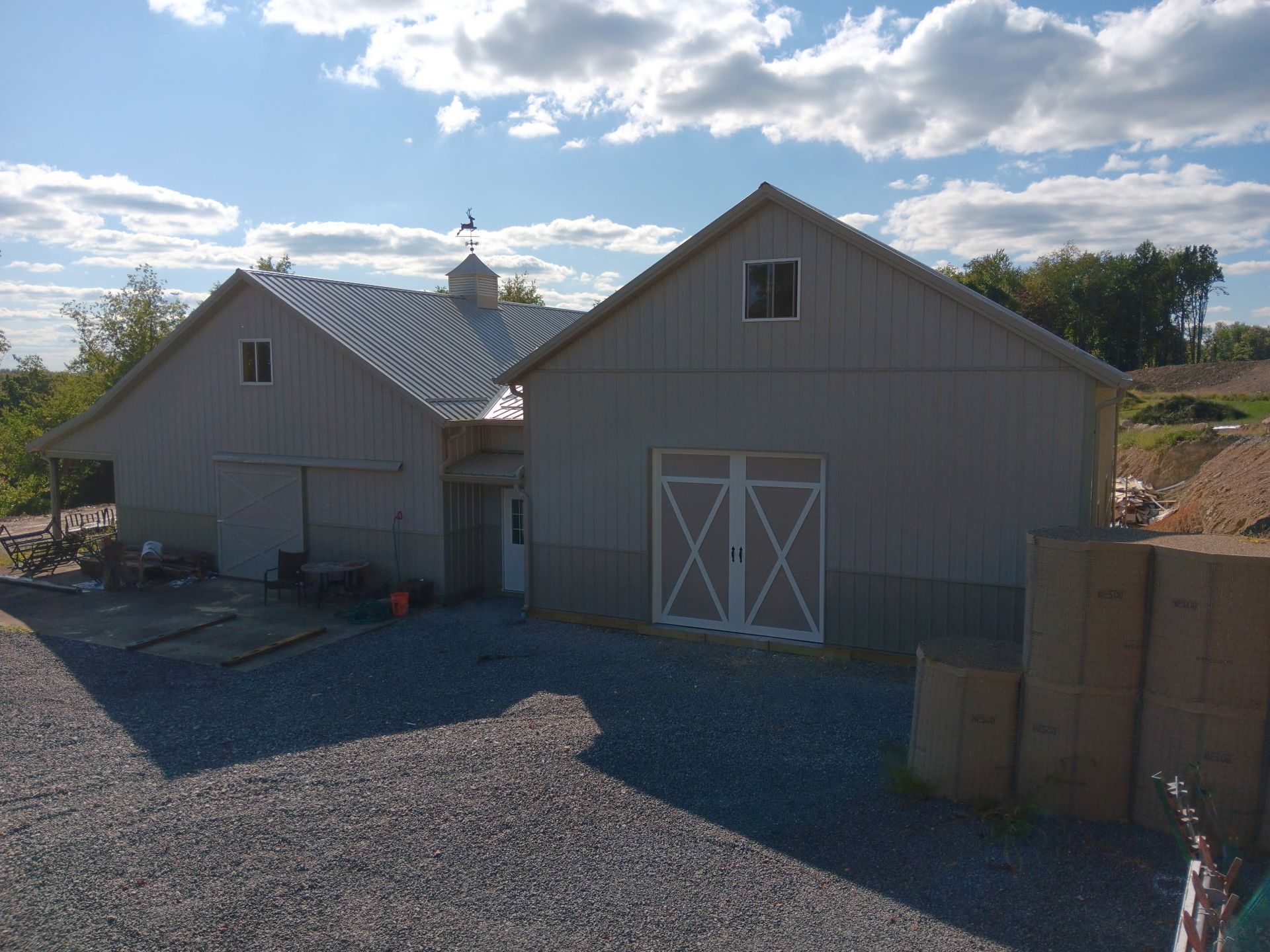 Gray barn-style building with metal roof and gravel yard under a partly cloudy sky