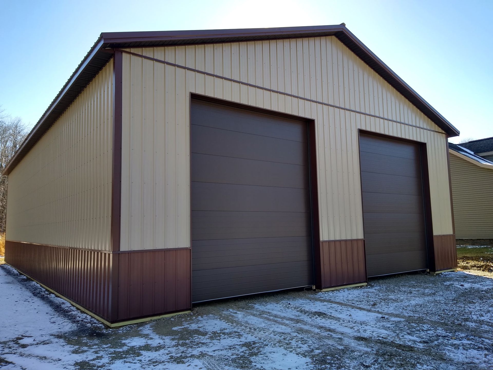 Tan metal storage shed with two large roll-up doors on a snowy lot