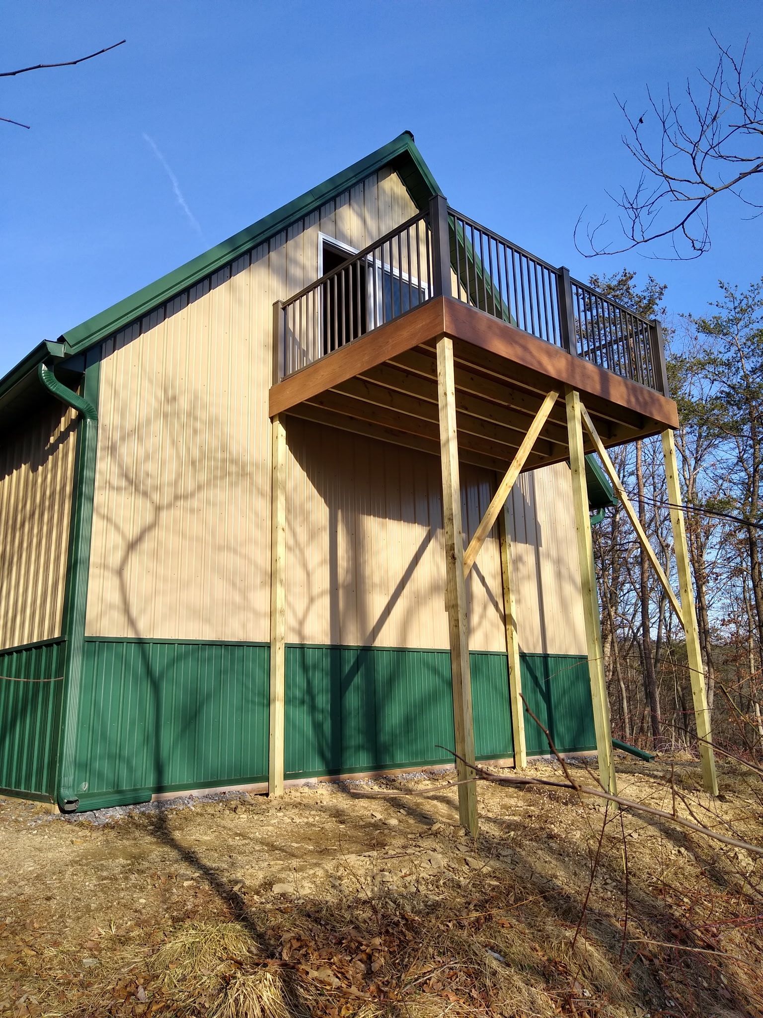 Tan-sided house with green trim and a small elevated wooden deck under a clear blue sky