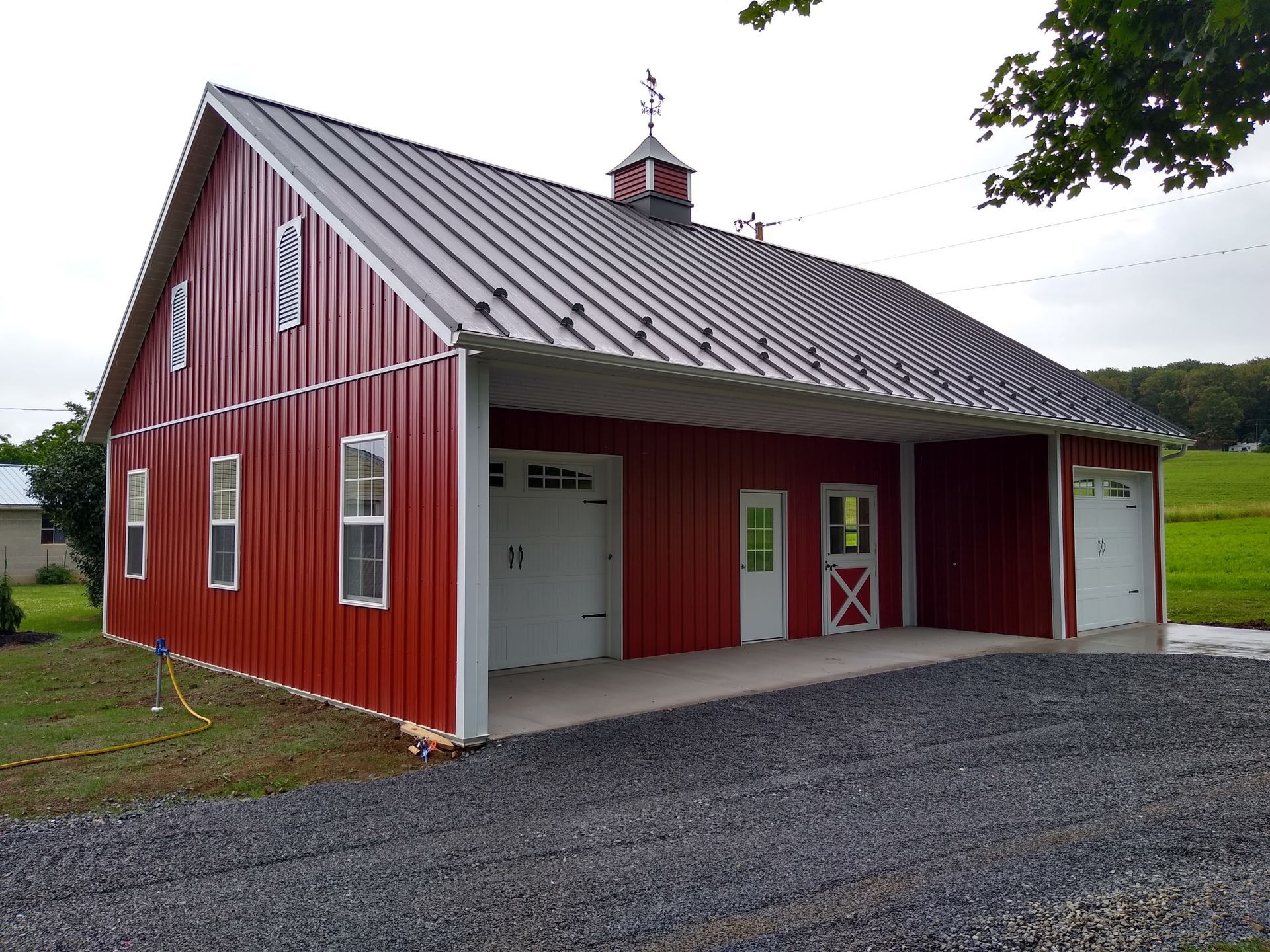 Red barn-style building with white trim, metal roof, and gravel driveway under overcast sky