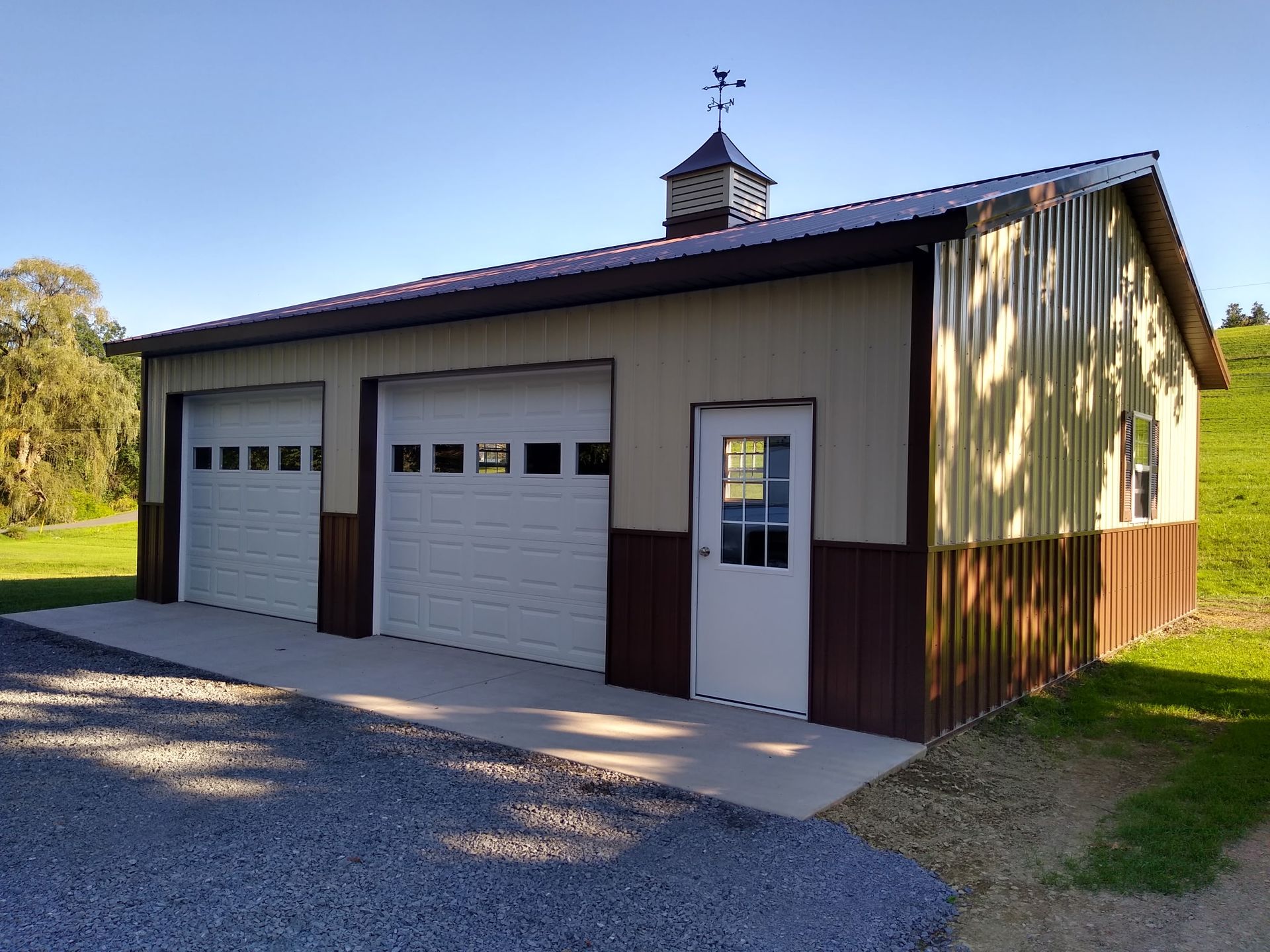 Two-car garage with white doors, brown trim, and a side entry door under a small cupola.