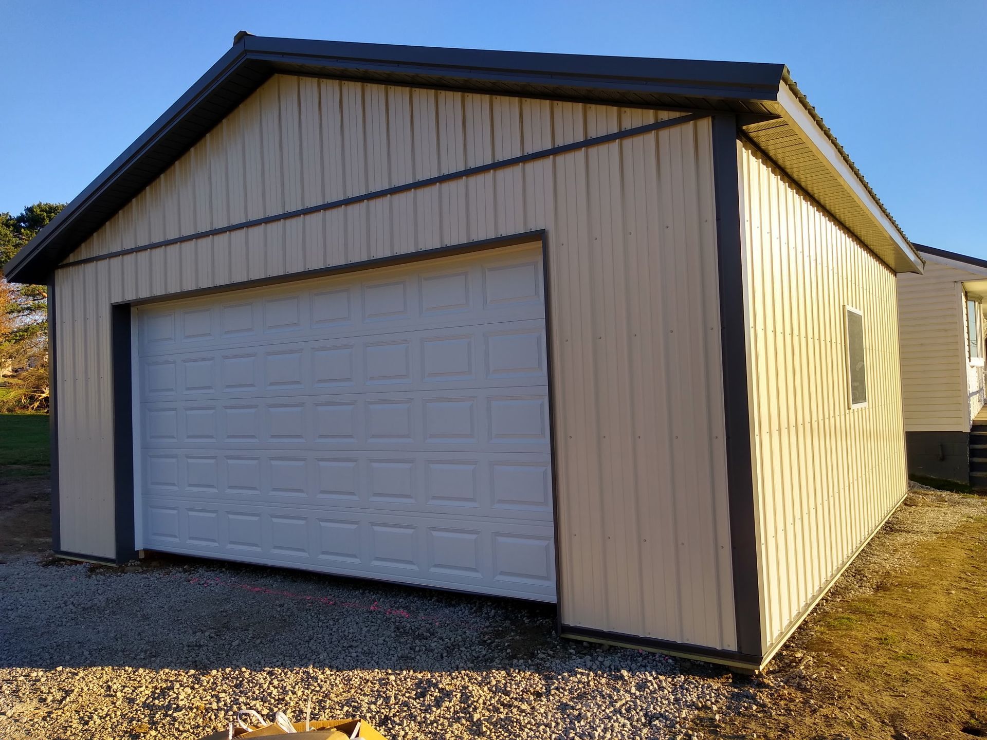 White garage with beige siding and a closed white door on a gravel driveway under a clear sky